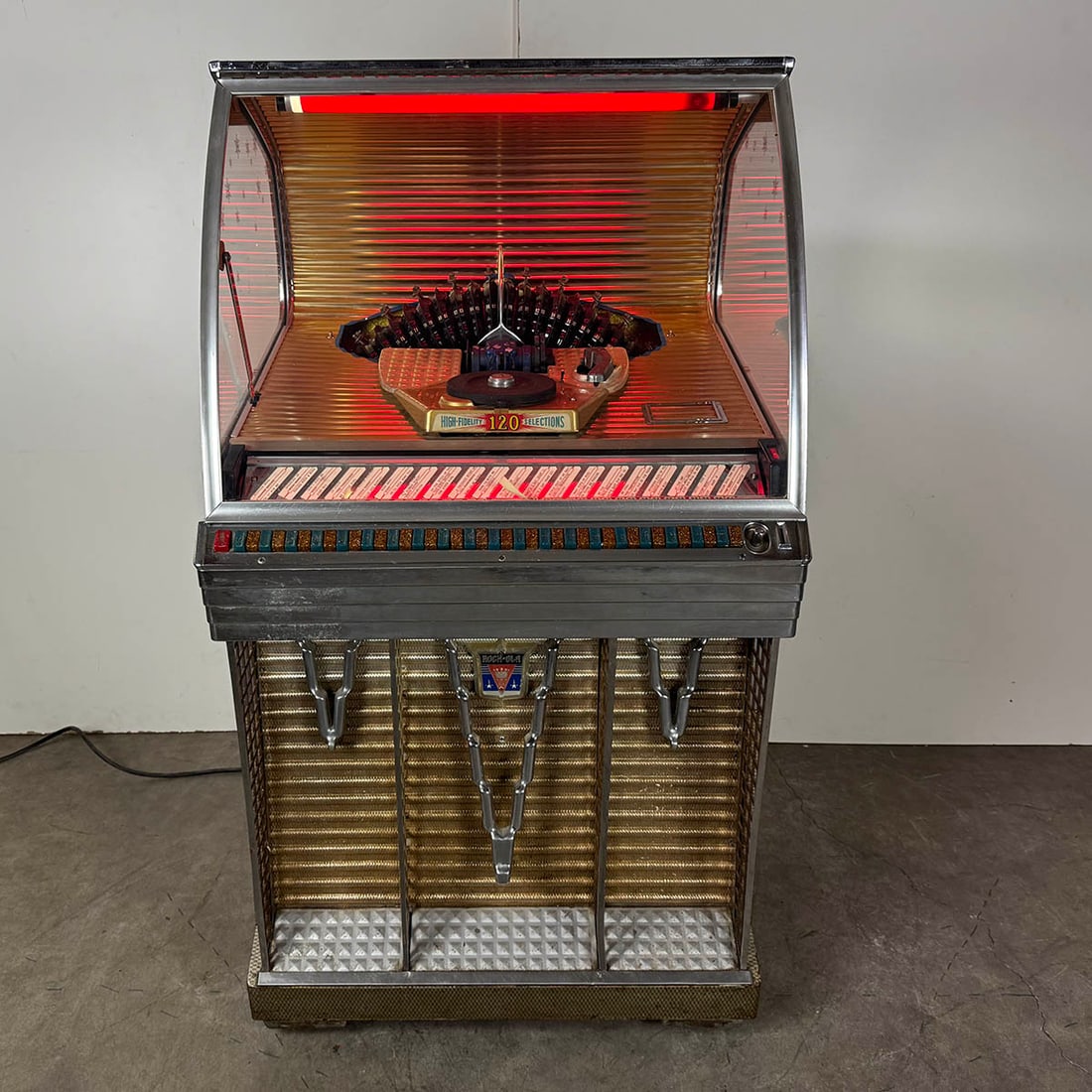 1956 Rock-Ola Model 1454 Jukebox: 1956 Rock-Ola Model 1454 jukebox. 120 selection jukebox playing 45 RPM records. Visual condition: good original visual condition, showing wear, some peeling of the side veneer. Missing the glass panel