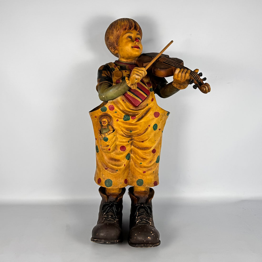 Large Coated Fiberglass Clown Sculpture Playing the Violin: This large coated fiberglass sculpture depicts a performing clown playing a violin. Good visual condition shows some wear and paint loss. Dimensions (H x W x D): 98 x 40 x 30 cm. Condition: Good. Loca