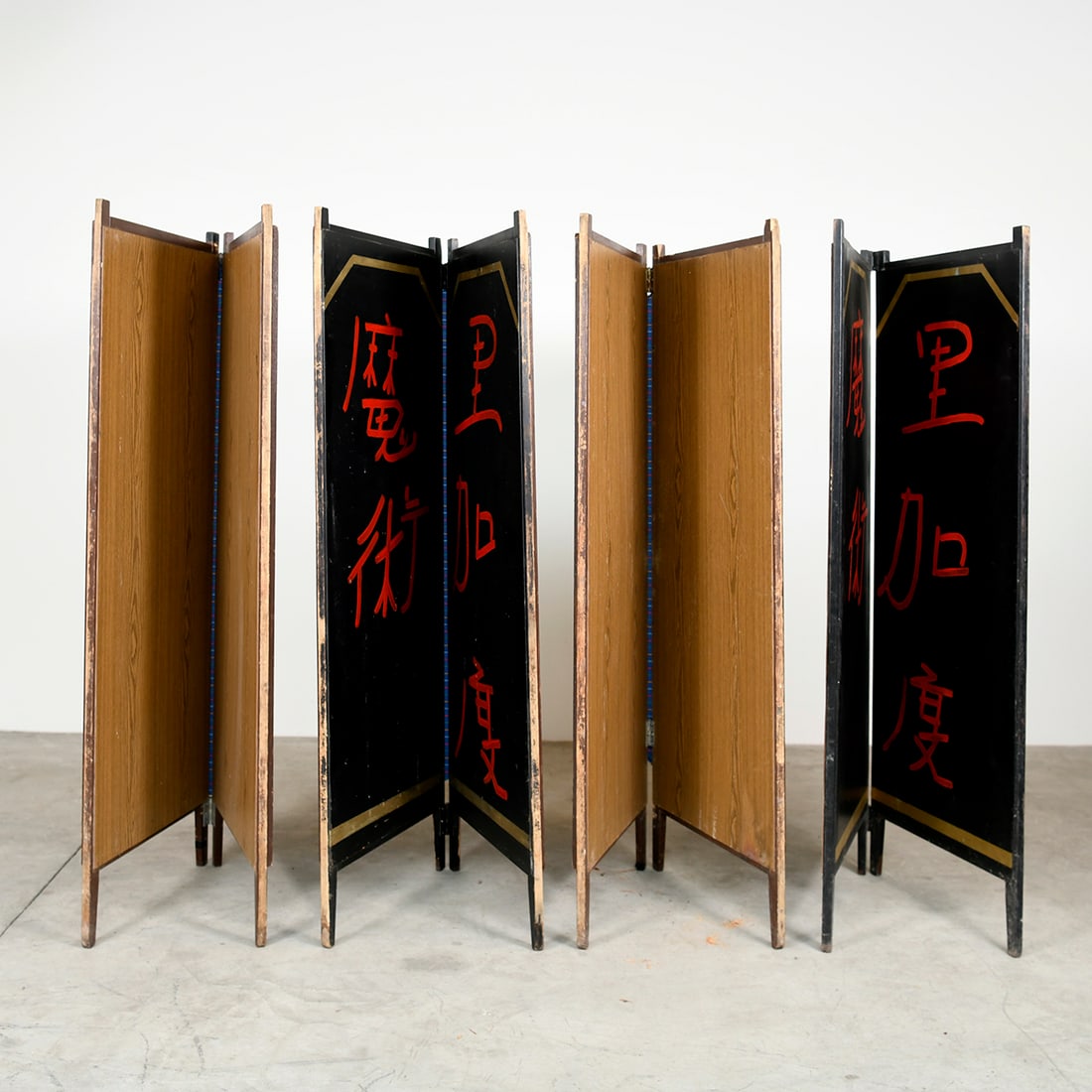 Set of 4 Wooden Folding Screens with 2 of the Screens Featuring Chinese-style Characters: Set of four folding screens constructed from wooden panels with hinged sections. Two of the screens feature black panels decorated with red Chinese-style characters and gold borders on one side, while