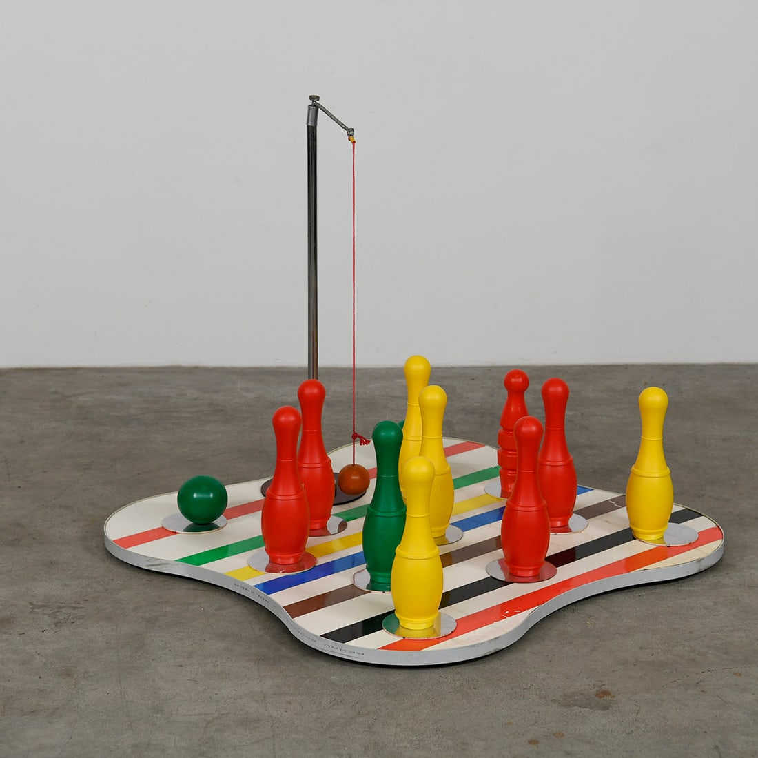 Fairground Skittles Bowling Game: Fairground Skittles or "swinging ball" bowling game featuring a multi-colored, striped base, several plastic pins in primary colors and a pair of green balls. Good visual condition showing some wear.