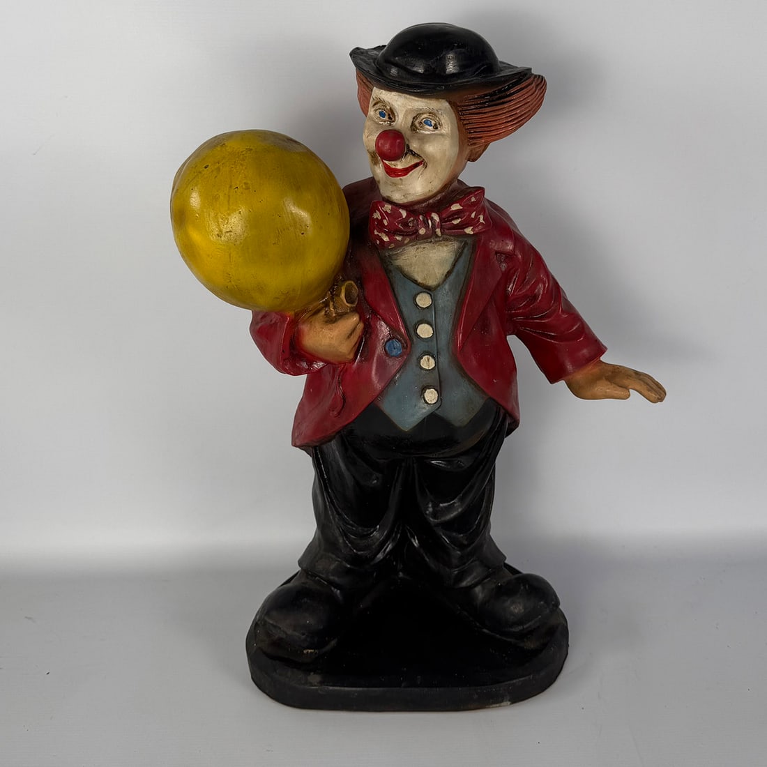 Clown with a Yellow Balloon: Decorative clown figure depicting a cheerful character holding a yellow balloon, dressed in a red jacket, bow tie and black hat. Colorfully painted and suitable as a circus-themed decorative piece.
