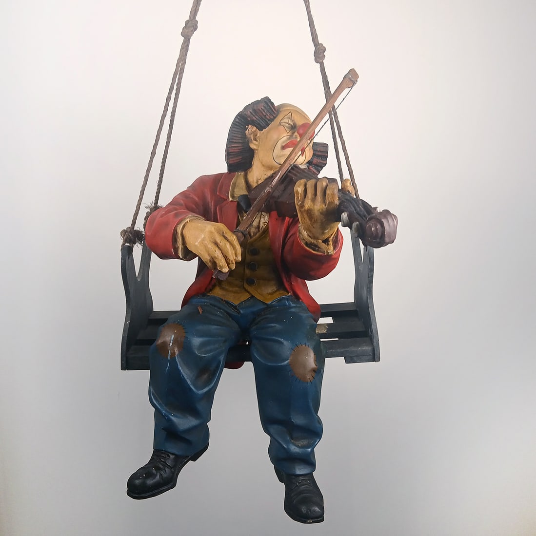 Large hanging clown with a violin, sitting on a bench: Decorative hanging clown figure depicting a clown seated on a small bench while playing a violin. The figure is suspended by ropes, creating a playful floating effect when displayed. Suitable for