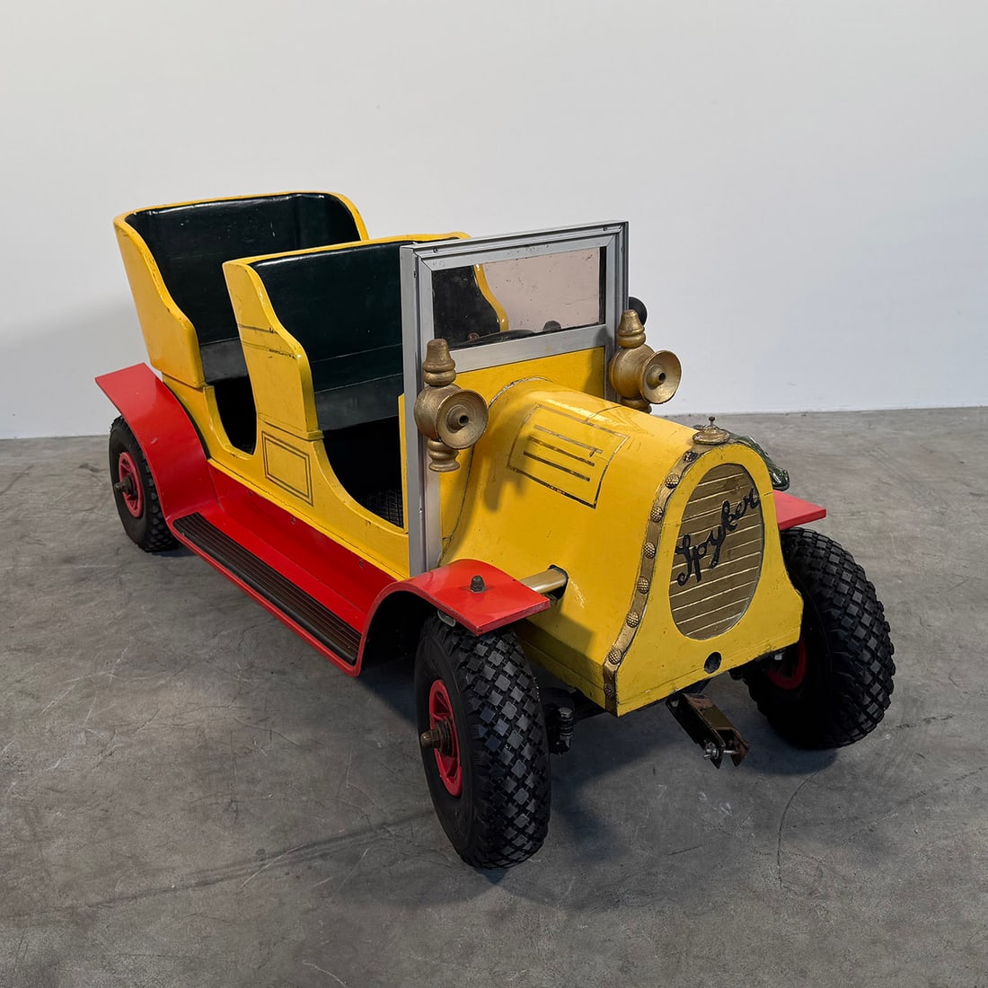 Vintage Toy Car Ride "Spyker": Vintage children’s ride-on toy car inspired by early 20th-century automobiles, featuring a distinctive design with two molded seats, a steering wheel, and decorative headlights. The body is finished
