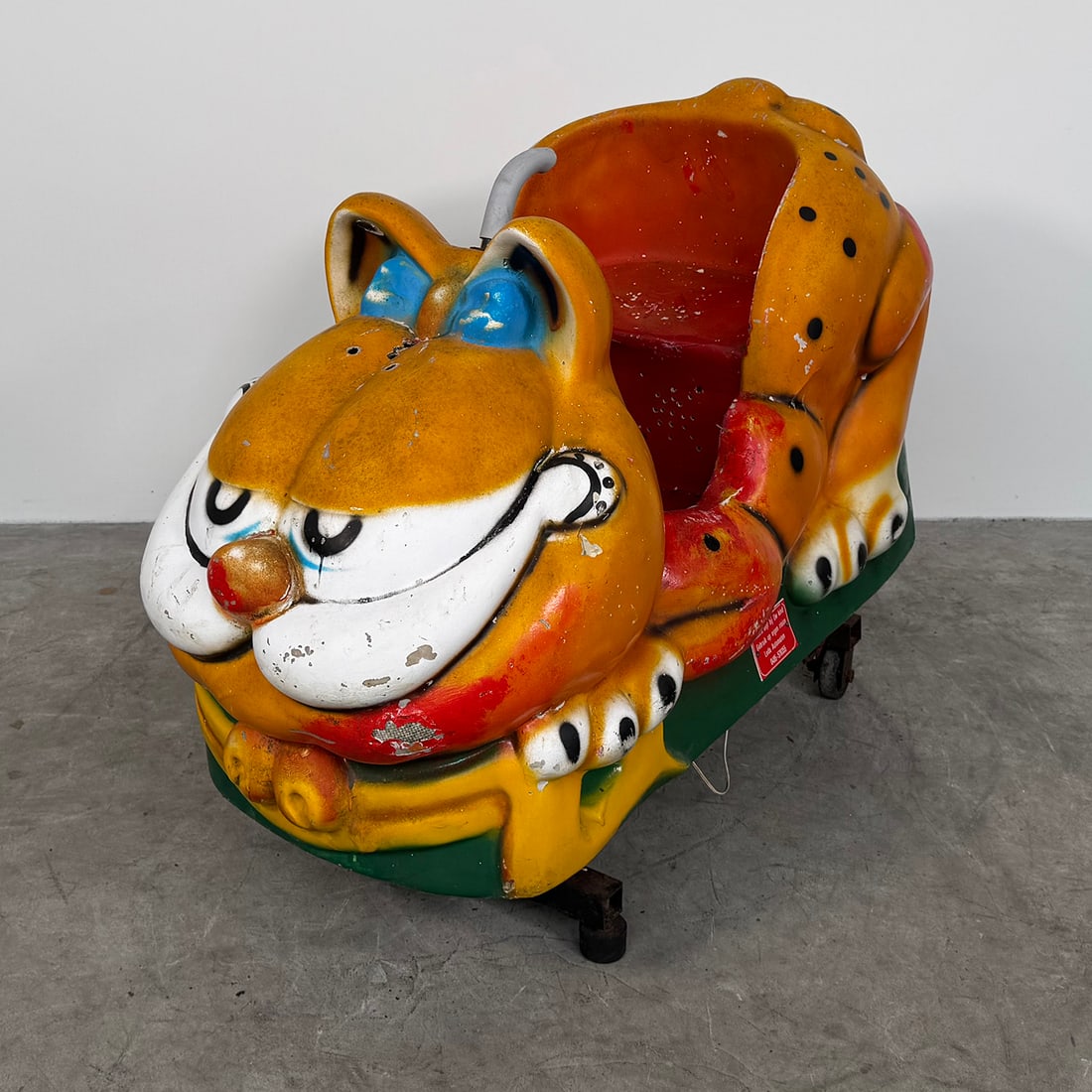 Garfield Kiddie Ride – Non-Working Condition: Vintage children’s amusement ride in the shape of the well-known cartoon character Garfield. The ride features a colorful molded body with Garfield’s characteristic orange color, black spots, and