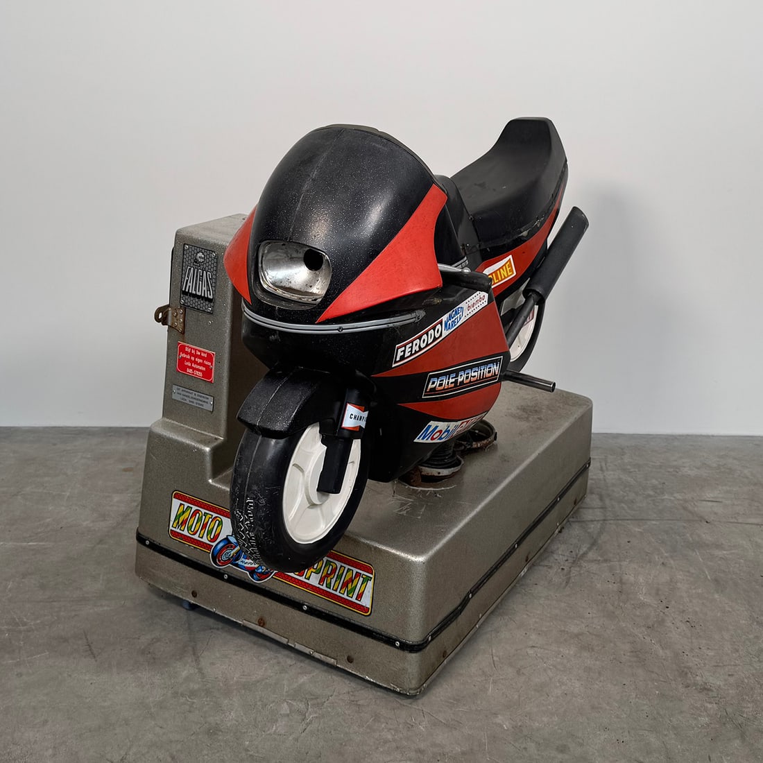 Moto Racer Kiddy Ride not working: Vintage children’s amusement ride designed in the shape of a racing motorcycle. The ride features a sporty black and red body with racing-style decals such as Ferodo, Valvoline, Pirelli, and Mobil,