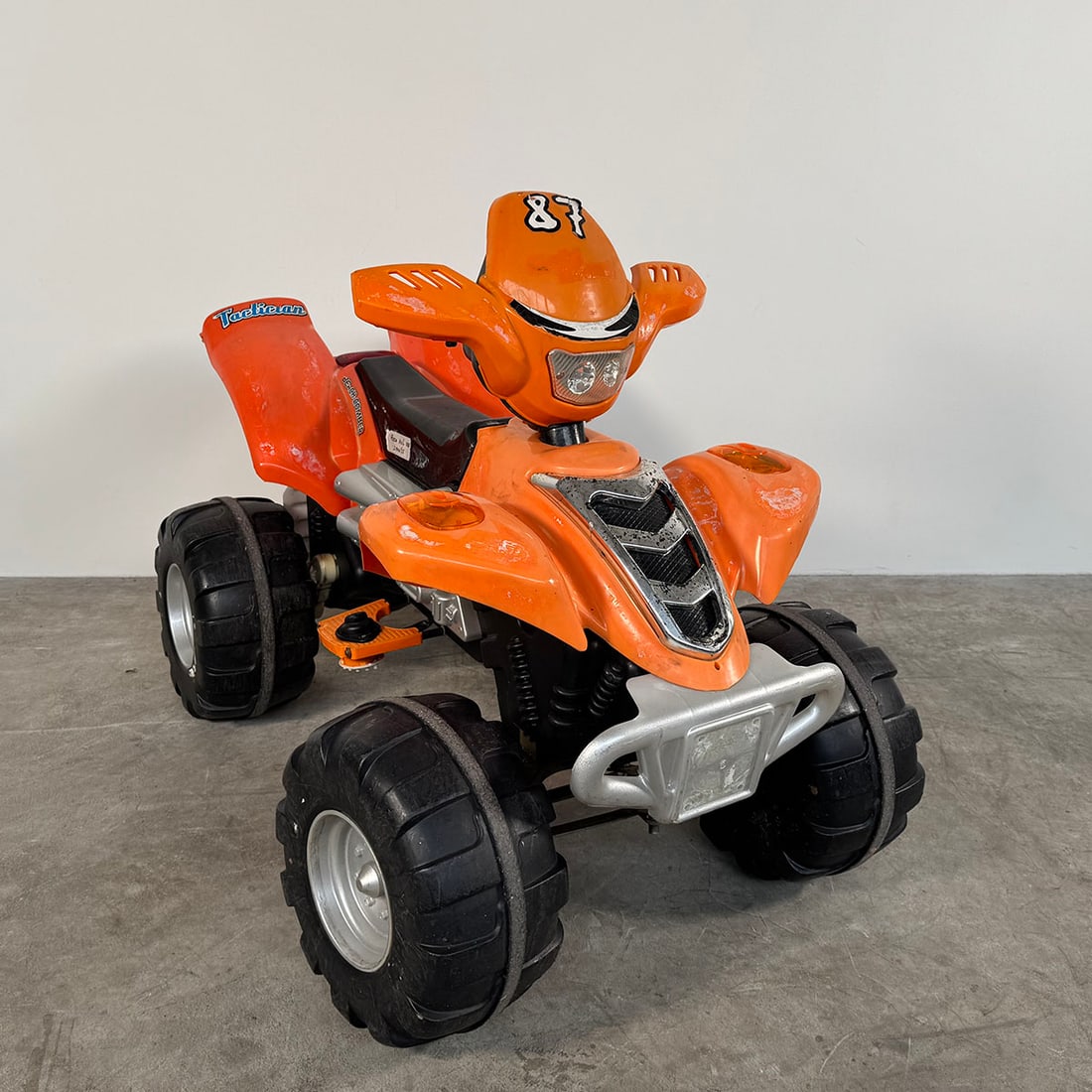 Electric Kids Quad Bike - Fully Working Condition orange color: Electric children’s quad bike in a bright orange color scheme with racing-style details and the number 87 on the front. The quad features large plastic wheels with rugged tread, a molded seat, handl