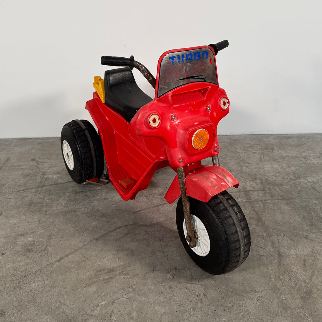 Vintage Red Turbo Electric Ride-On Motorcycle for Kids ( with charger): Vintage children’s electric ride-on motorcycle with a bright red plastic body and a stable three-wheel design. The model features a molded seat, handlebars for steering, and large plastic wheels. Th
