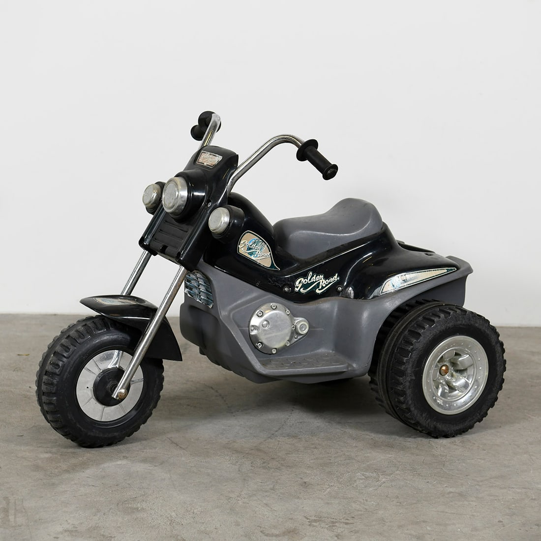 1 black trike motorcycle (plastic) with a new 12-volt battery and plug-in charger: Vintage children’s electric ride-on motorcycle with a classic chopper-style design. The vehicle features a black and grey body with “Golden Road” branding, a wide front fork, and three wheels fo