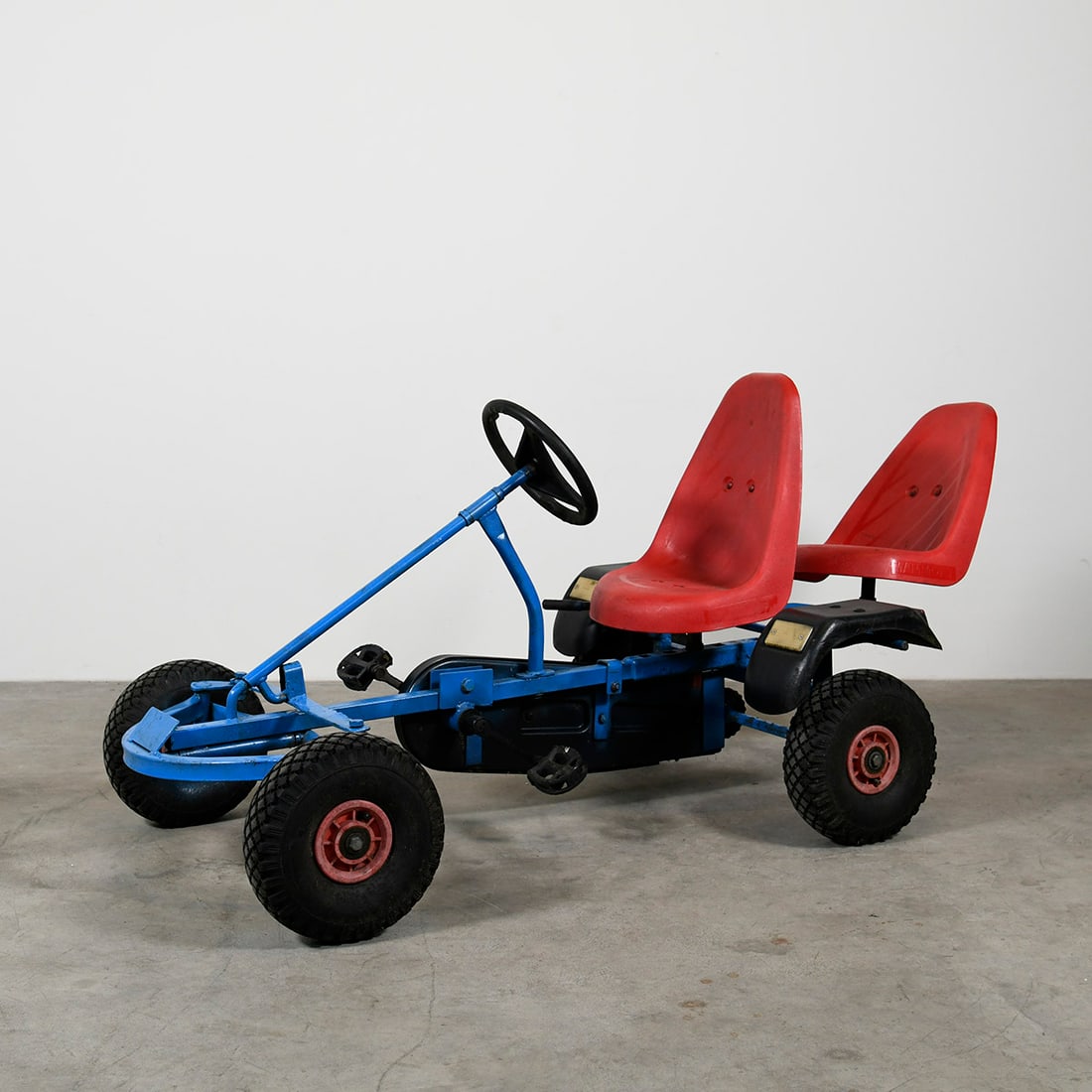 2-person pedal go-kart, blue, brand BERG: Vintage children’s pedal go-kart with a sturdy metal frame and seating for two. The vehicle features a driver’s seat with steering wheel and pedals, along with a second passenger seat at the rear.