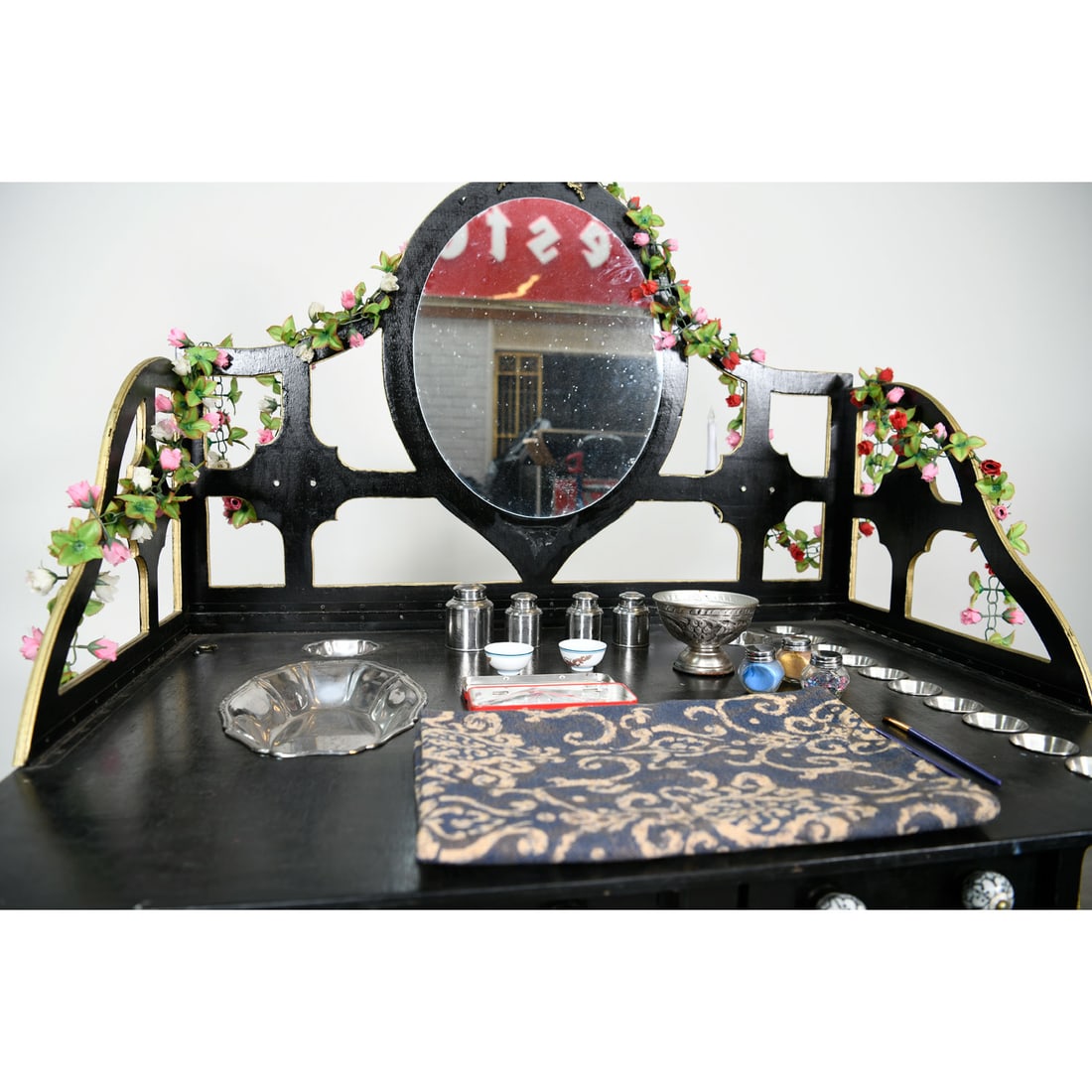 Gothic Style Wooden Vanity Makeup Table Used by Royce and Mariandl: This piece is a gothic-inspired wooden vanity makeup table, constructed with a black frame and intricate gold-lined geometric fretwork along its base and sides. The upper section features an oval mirr