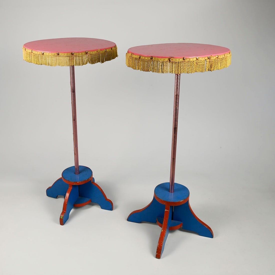 Set of 2 Vintage Magician's Tables: This pair of vintage magician's tables features a vibrant stage aesthetic defined by circular pink tops bordered with gold-toned fringe and decorative metal studs. The central supports consist of slen