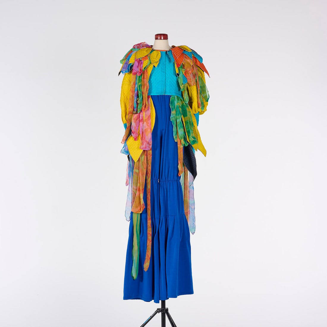 Original Stilt Act Costume with Blue Base and Colorful Leaf-like Layers from the Royce Collection: This colorful stilt act costume from the Royce Collection features an elongated, vibrant silhouette characterized by a saturated royal blue base and an explosion of colorful, textured layers. Please u