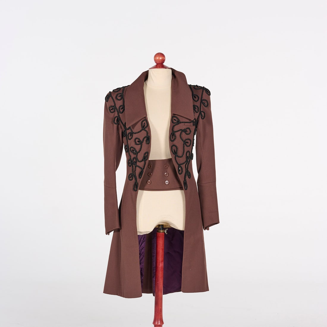 Original Tailored Frock Coat with Black Braided Cord Embroidery from the Royce Collection: This tailored, mid-length frock coat from the Royce Collection is crafted from a chocolate brown fabric and features an open-front design with structured shoulders and wide, peaked lapels. The garment