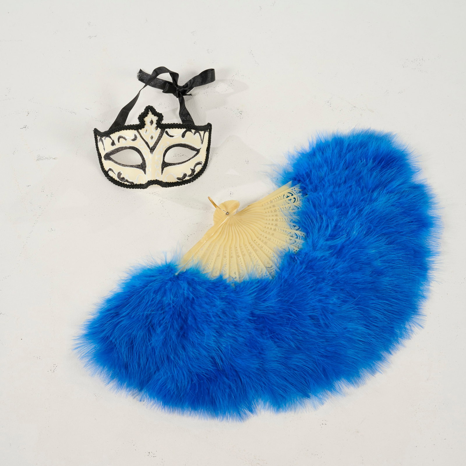 Decorative Mask and Fan Set from the Royce Collection: Shimmering masquerade mask and a vibrant, blue feather fan from the Royce collection. The mask is decorated with black glitter patterns, finished with a black trim and black ribbon. The accompanying f