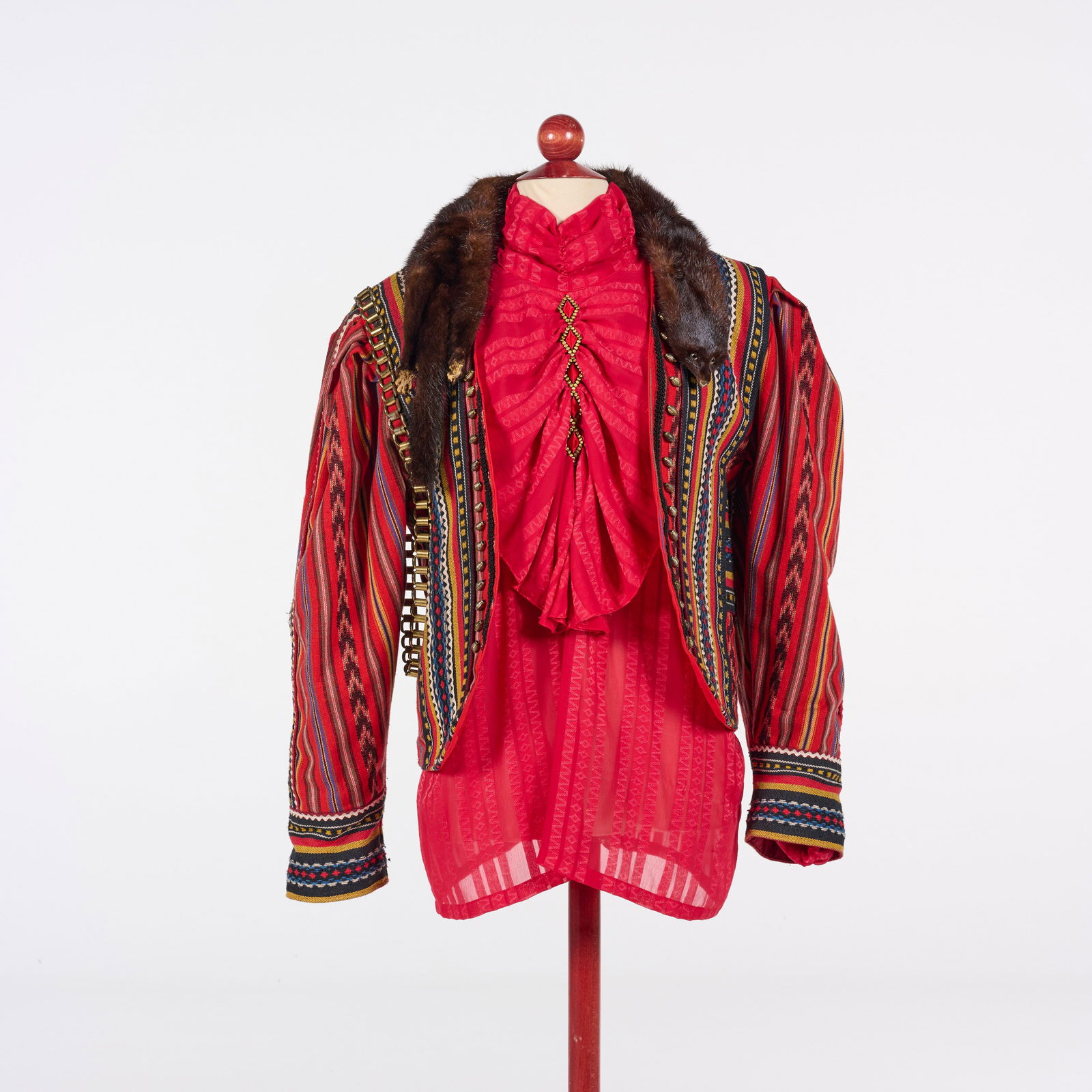 Traditional Folk-inspired Costume from the Royce Collection: This vibrant traditional folk-inspired costume from the Royce Collection features a red ruffled blouse layered under a short jacket with bold vertical stripes in red, yellow, blue, and black, and embr