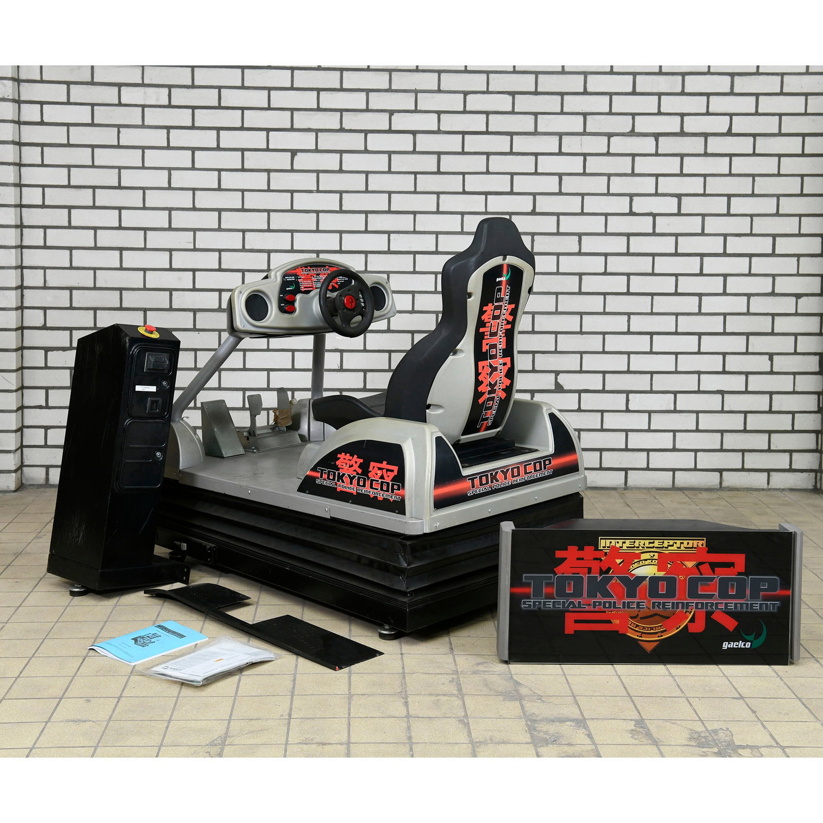 Tokyo Cop Special Police Reinforcement Arcade Game Parts Gaelco (2003): This is a lot of Tokyo Cop Special Police Reinforcement arcade game parts by Gaelco, produced in 2003. The cabinet is a motion simulator type with a black racing seat and a grey frame featuring 'Tokyo