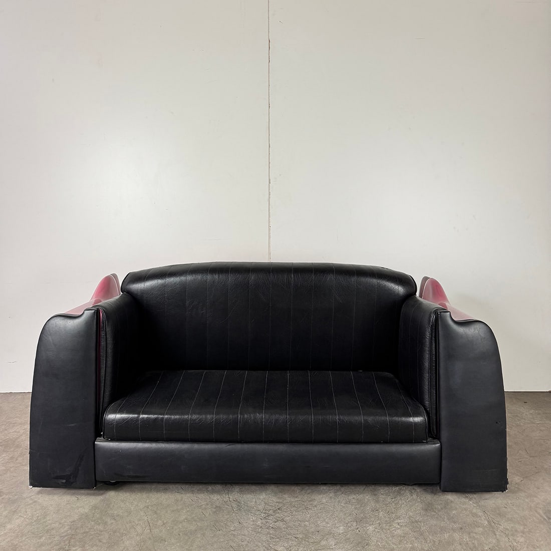 Contemporary Couch with Black Vinyl Tufting and Pink 1955 Cadillac Fleetwood Back Design: Contemporary couch with black vinyl tufting and a pink 1955 Cadillac Fleetwood back design. The rear of the couch is constructed from fiberglass and features a chromed metal bumper. The piece is in ve