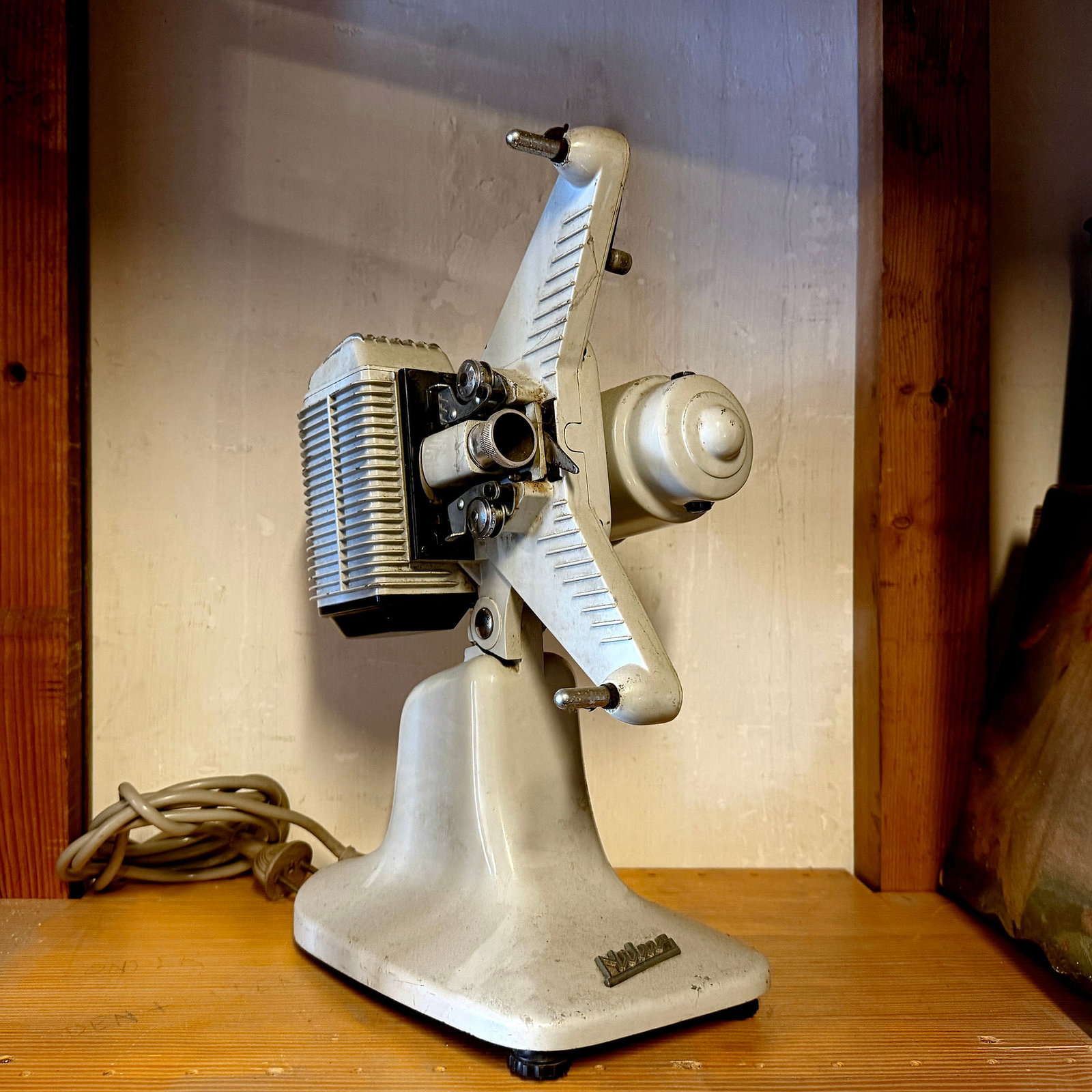 Eumig P8 8mm Film Projector (c. 1954-1960s): This vintage Eumig P8 8mm film projector features a light grey/off-white casing with visible signs of age including dust accumulation and minor surface scuffs consistent with historical use. The base 