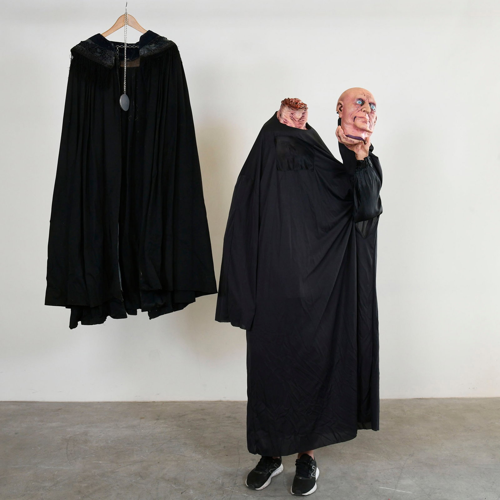 Headless Man Horror Costume & Cape with Pentagram Pendant: Headless man horror costume & cape with pentagram pendant. The black cape shows significant wear; its internal lining is extensively torn, frayed, and detached in multiple areas, with visible damage a