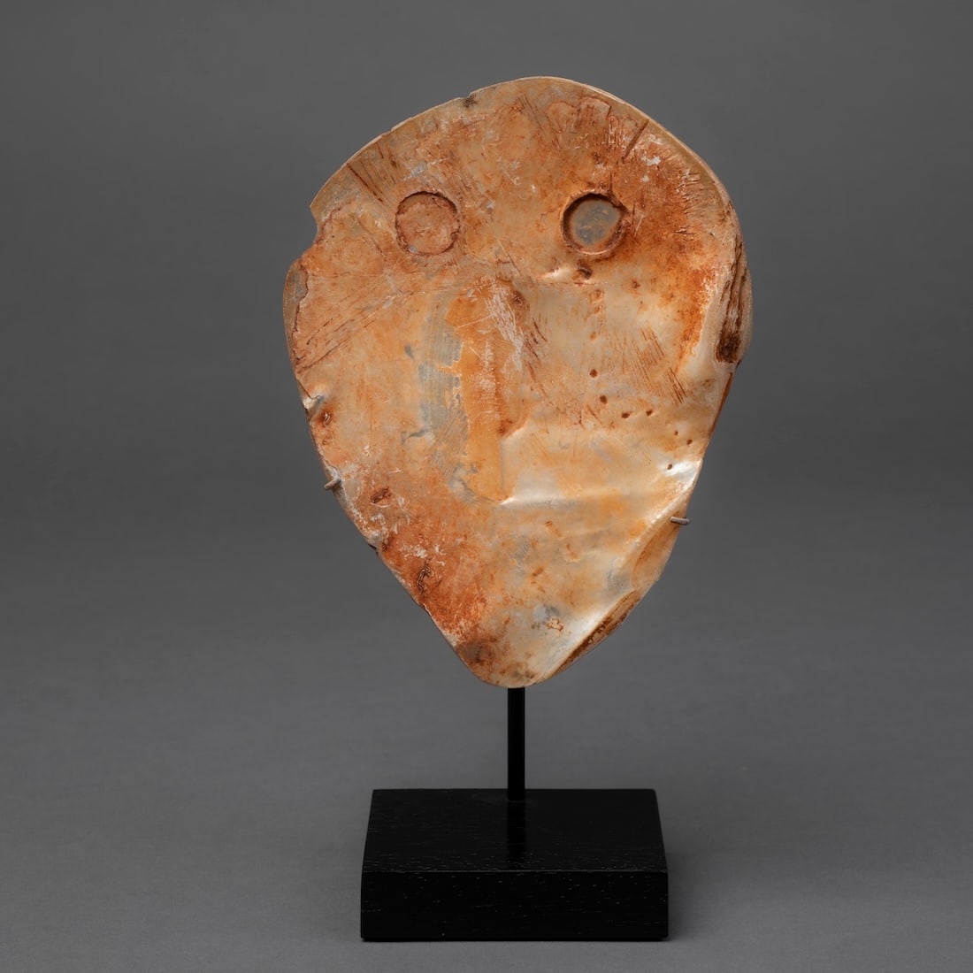 An Australian Aborigine shell: The pearl shell with two round “eyes” at the top, with traces of red ochre, mounted on a wood base, (two chips to the rim). Ht. 6 1/4, wd. 4 5/8 in. Provenance: Private collection, Santa Fe, N