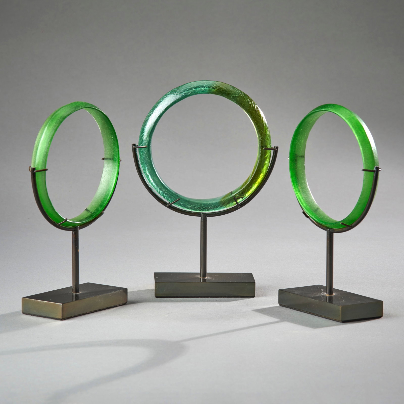 Three Dong Son Glass Bracelets: Southeast Asia, circa 200 BC/200 A.D., the largest with incised hatch work on the exterior, each of carinated form, and mounted on a custom base. In good condition. Dia. 3 3/4 in. 9.5 cm, dia. 3 5/8 i