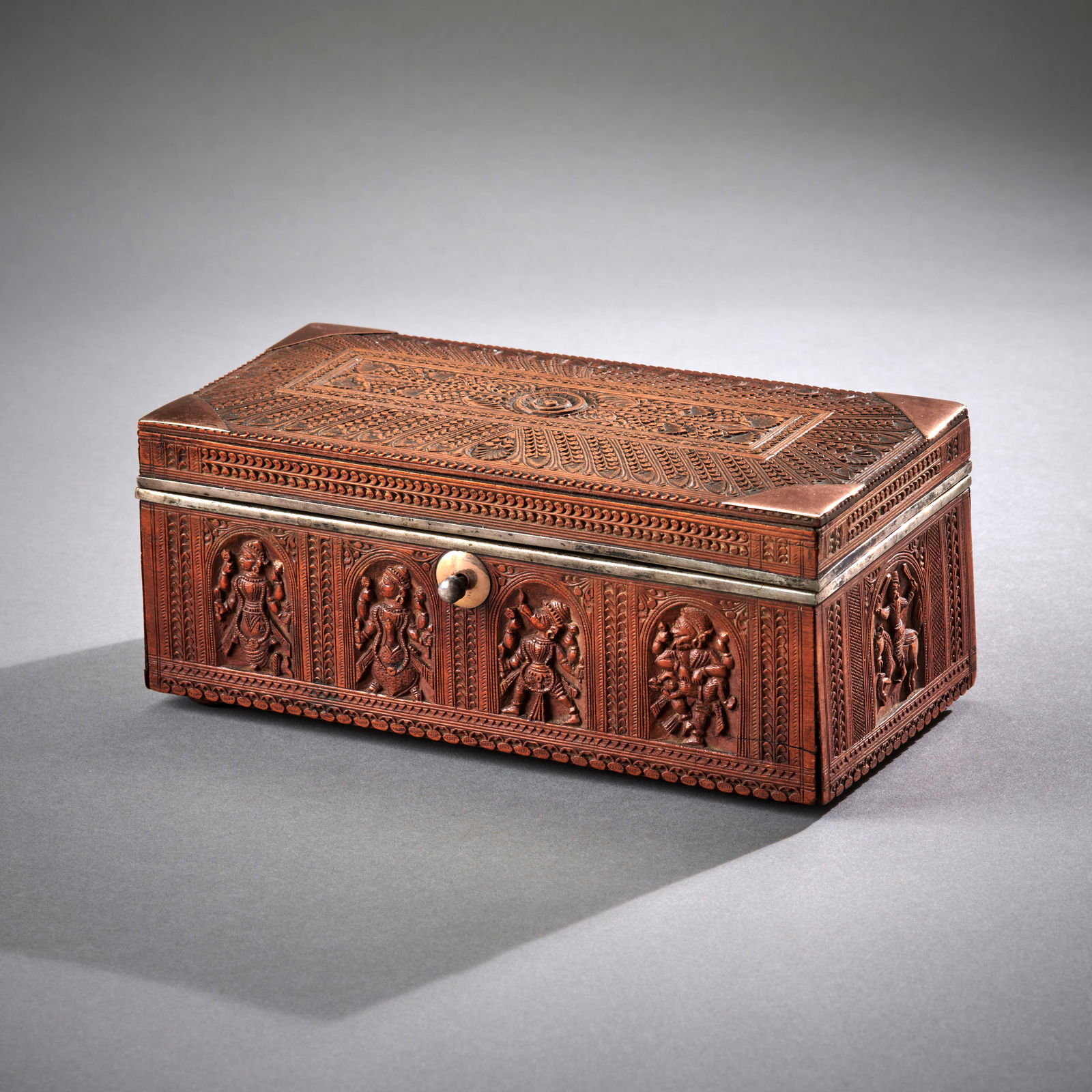 A South Indian Wood Box: 19th century, a fine sandalwood box the sided decorated with various deities in arched niches, the lid decorated with linear and legal motifs, with silver mounts. The lid with horizontal crack at rear