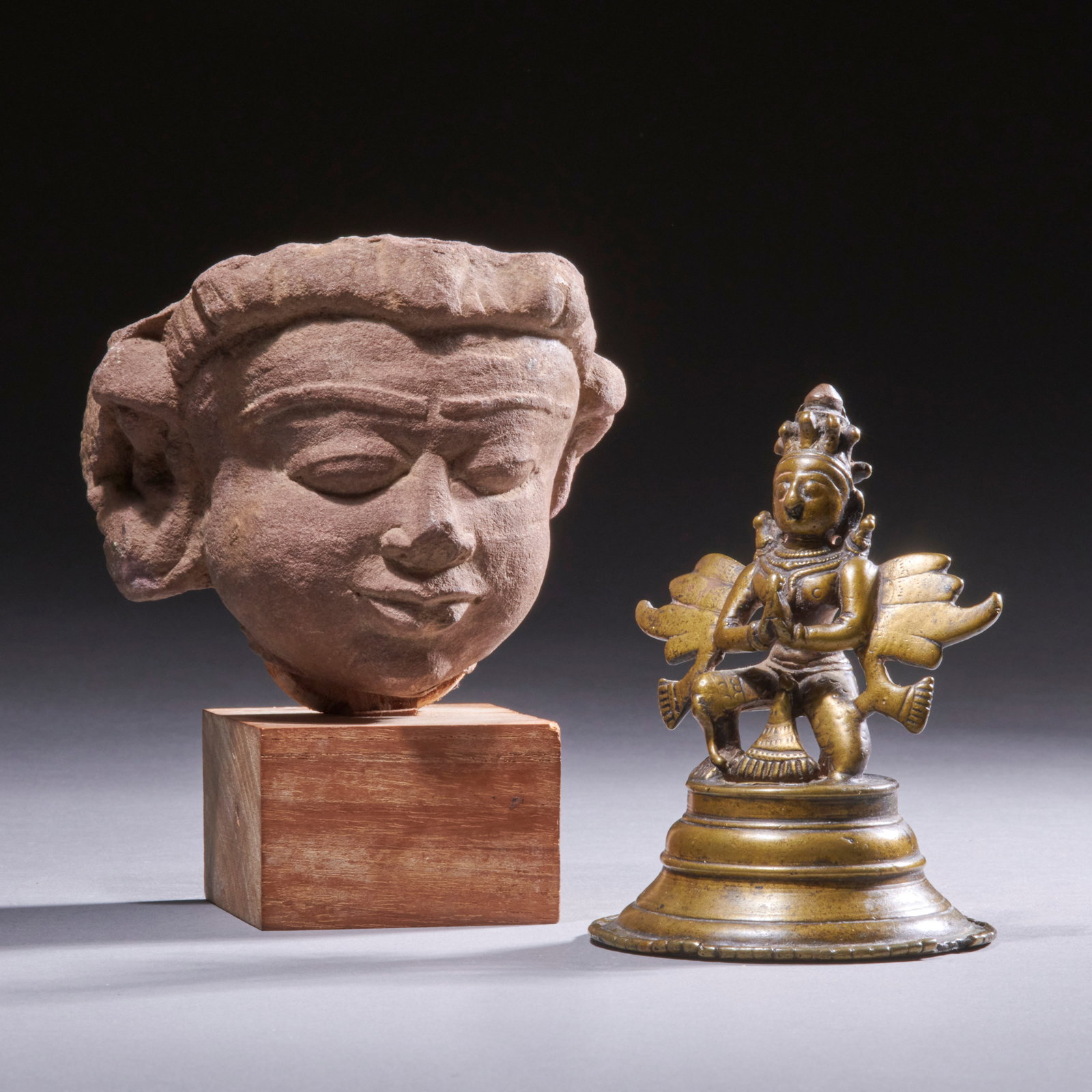 Two Indian Objects: Central India, circa 13th and 18th century, a pink sandstone head of a youthful male, mounted on a wood block along with a bronze figure of Garuda on tiered round base. Bronze is 4 in. high. Stone hea