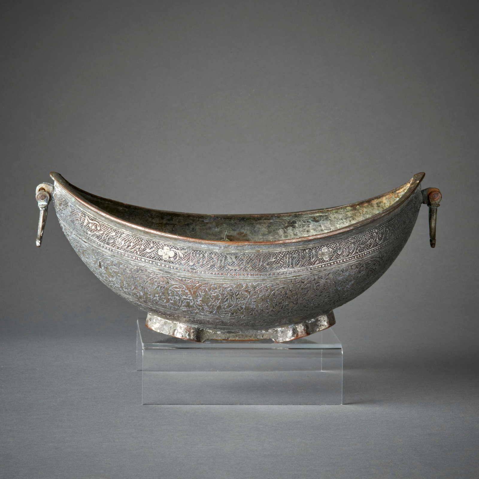 A Silvered Copper Kashkul: 19th century, the begging bowl of typical form, engraved with floral scrolls and Islamic script, the interior with inlaid silver decorations. Lg. 10 1/4 in. Shipping within the continental U.S. is $35