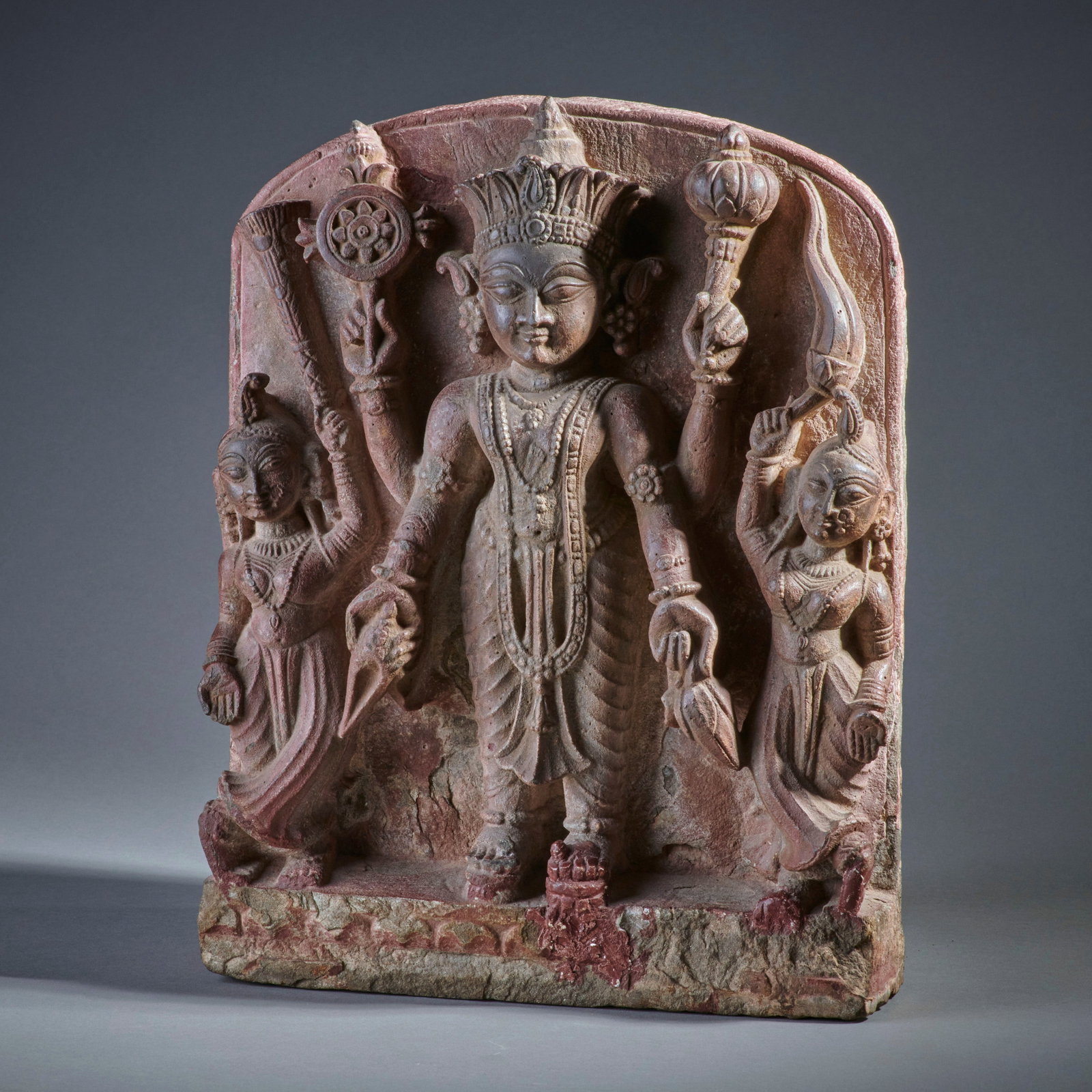 A Nepalese Stone Vishnu stele: Circa 18th/early 19th century, a charming depiction of Vishnu flanked by two female attendants, some of the surface with remains of red pigment from worship. Losses to some figures’ toes, otherwise 
