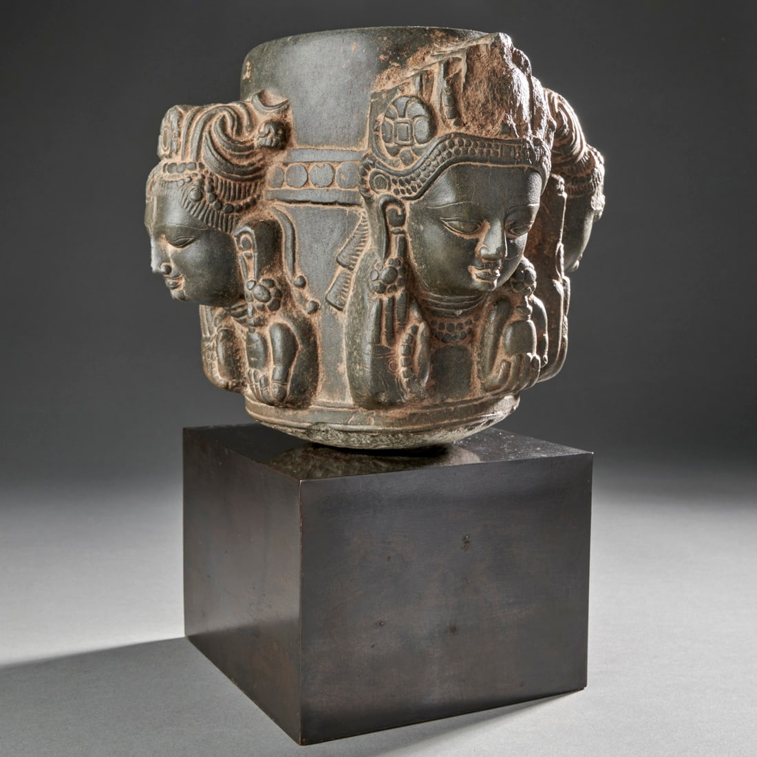 A Fine Nepalese stone Linga: Nepal, 12th-13th century, a rare and refined fragment of a four headed linga (Caturmukhalinga) carved in grey schist. It depicts each of the four faces of Shiva’s manifestations with a pair of hands