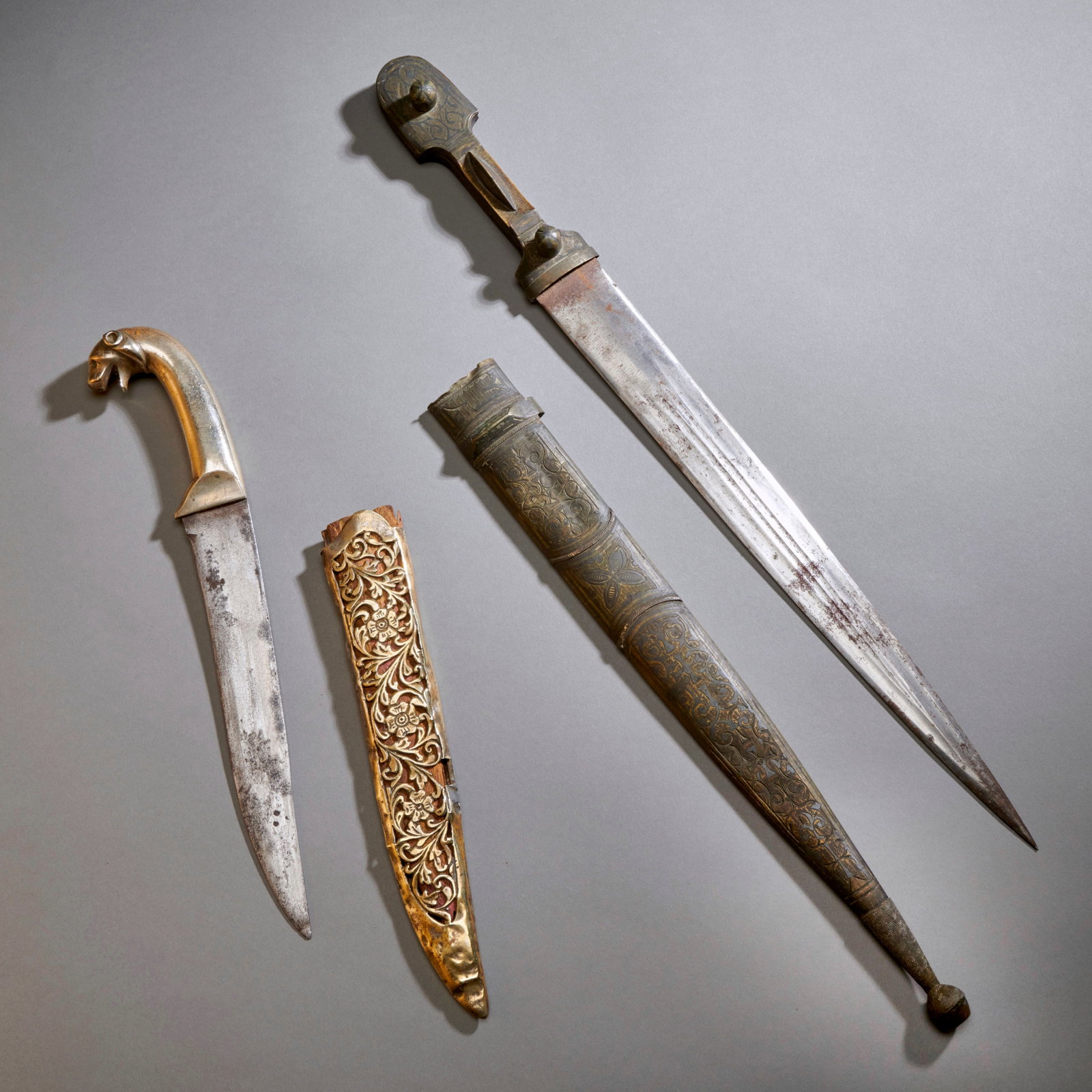 Two Indo Persian Knives: 19th century, the Khanjar with lion pommel with openwork floral decorated scabbard. Lg. incl scabbard 13 in. 33 cm. The Kindjal the handle with silver niello work, the blade with twin blood grooves. T