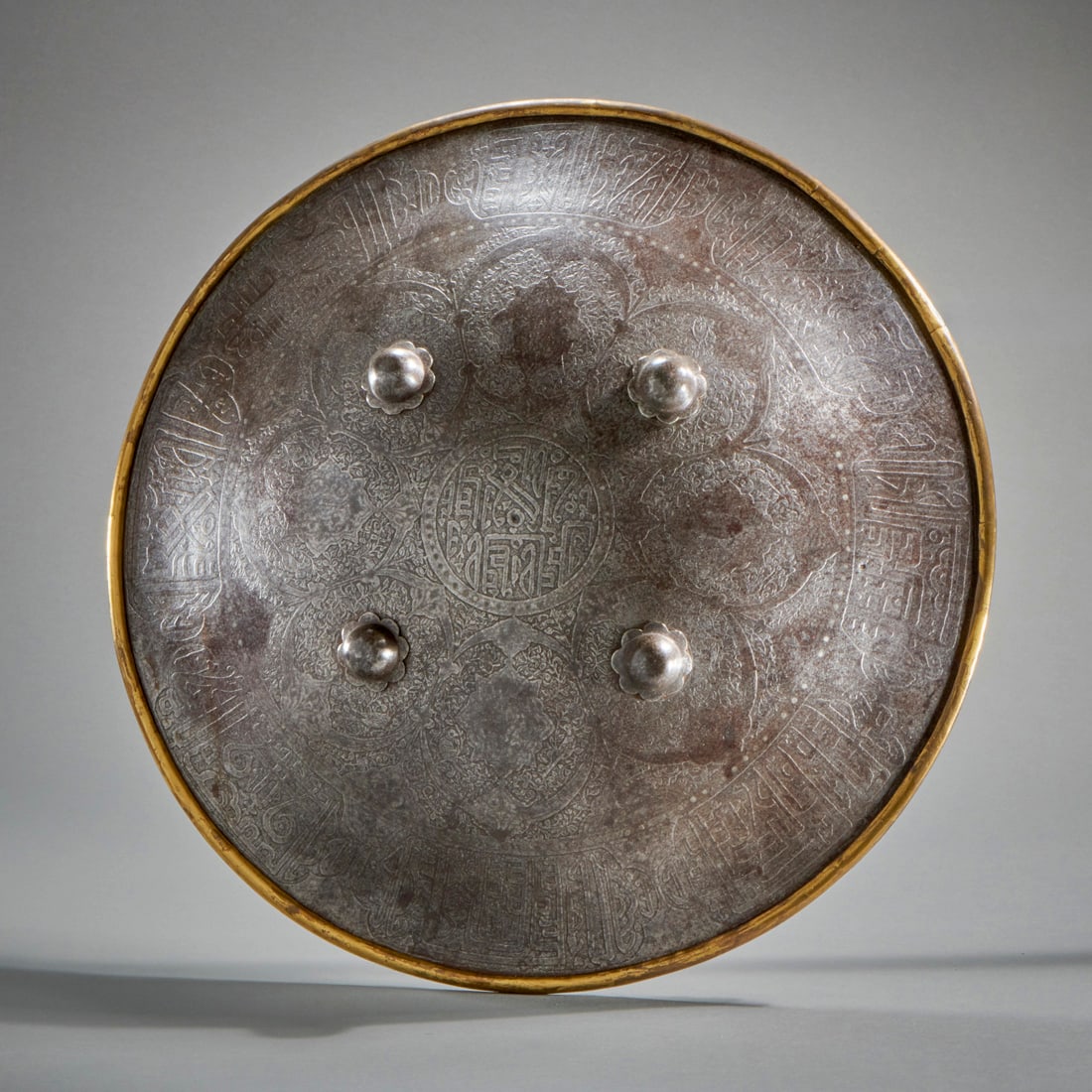 An Indo Persian Shield: 19th century, finely engraved with foliate and calligraphic elements, with an applied brass rim. Good condition, as shown. Dia. 18 1/4 in. Shipping within the continental U.S. is $60 plus insurance.