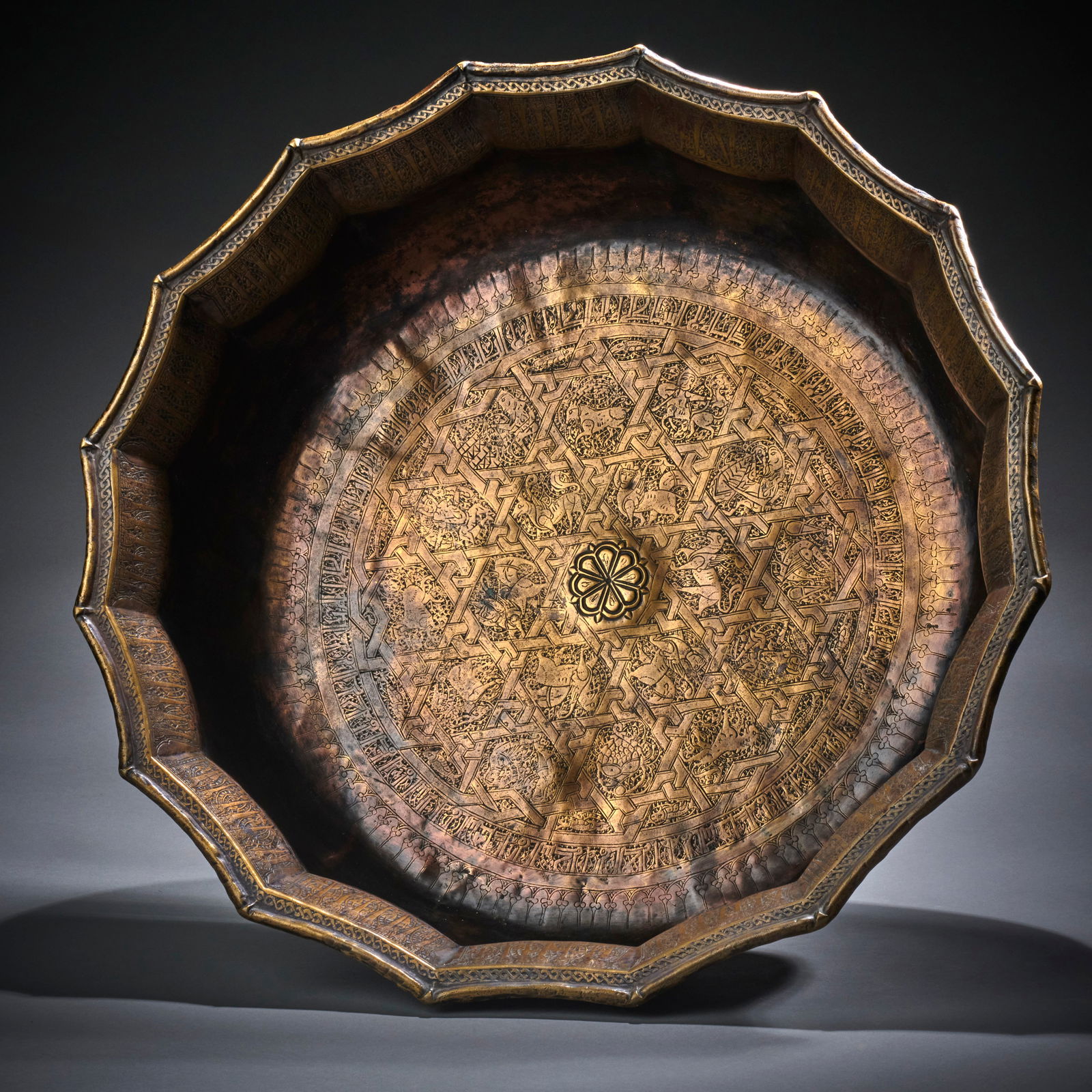 A Very large Khorasan Brass Basin: Afghanistan, second half of 12th century, with flat base, the sides curving inwards and then flaring outwards, with very finely incised decoration, the base with a stellar interlace containing figural