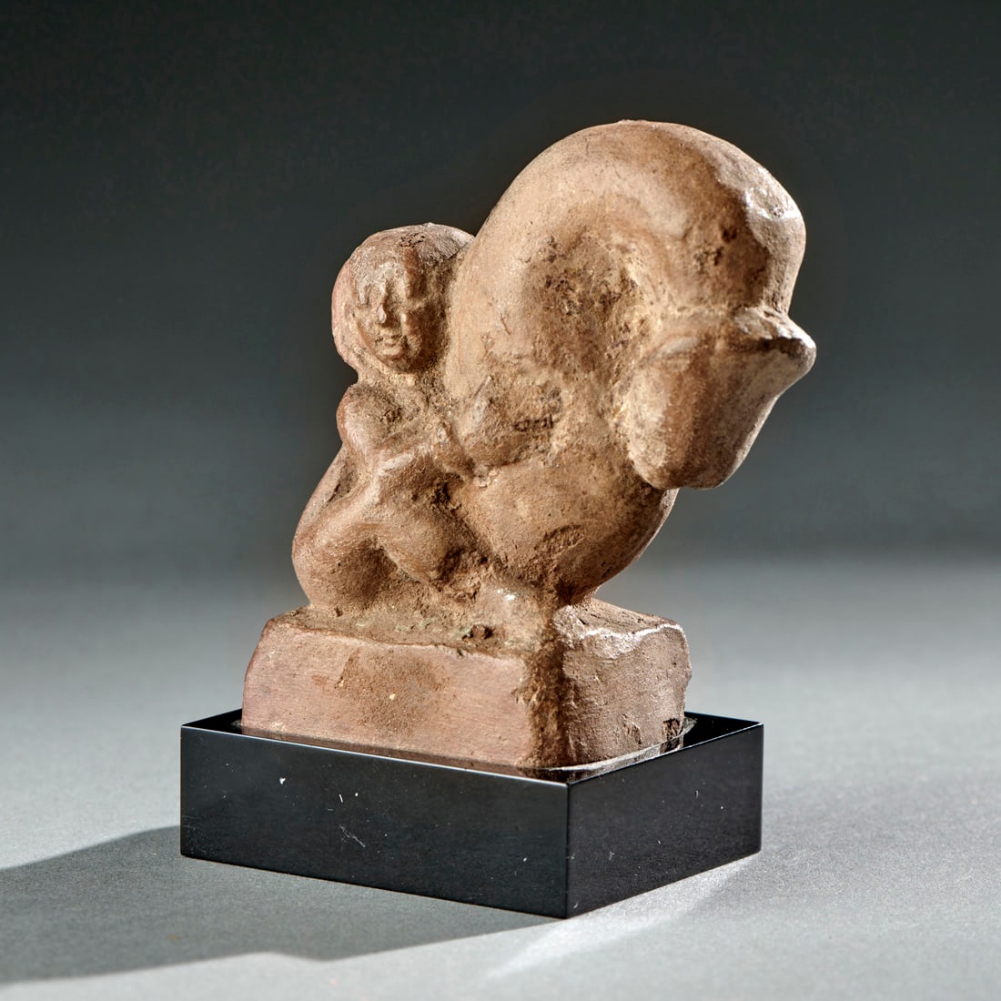 A Terracotta Figure Of Harpocrates: Alexandrian, circa 1st century B.C., the youthful, seated god grasping his enormous phallus with both hands, on custom base. Ht. 2 3/4, 3 1/4 in. with base. Provenance: Purchased at Sotheby’s NY, Ju