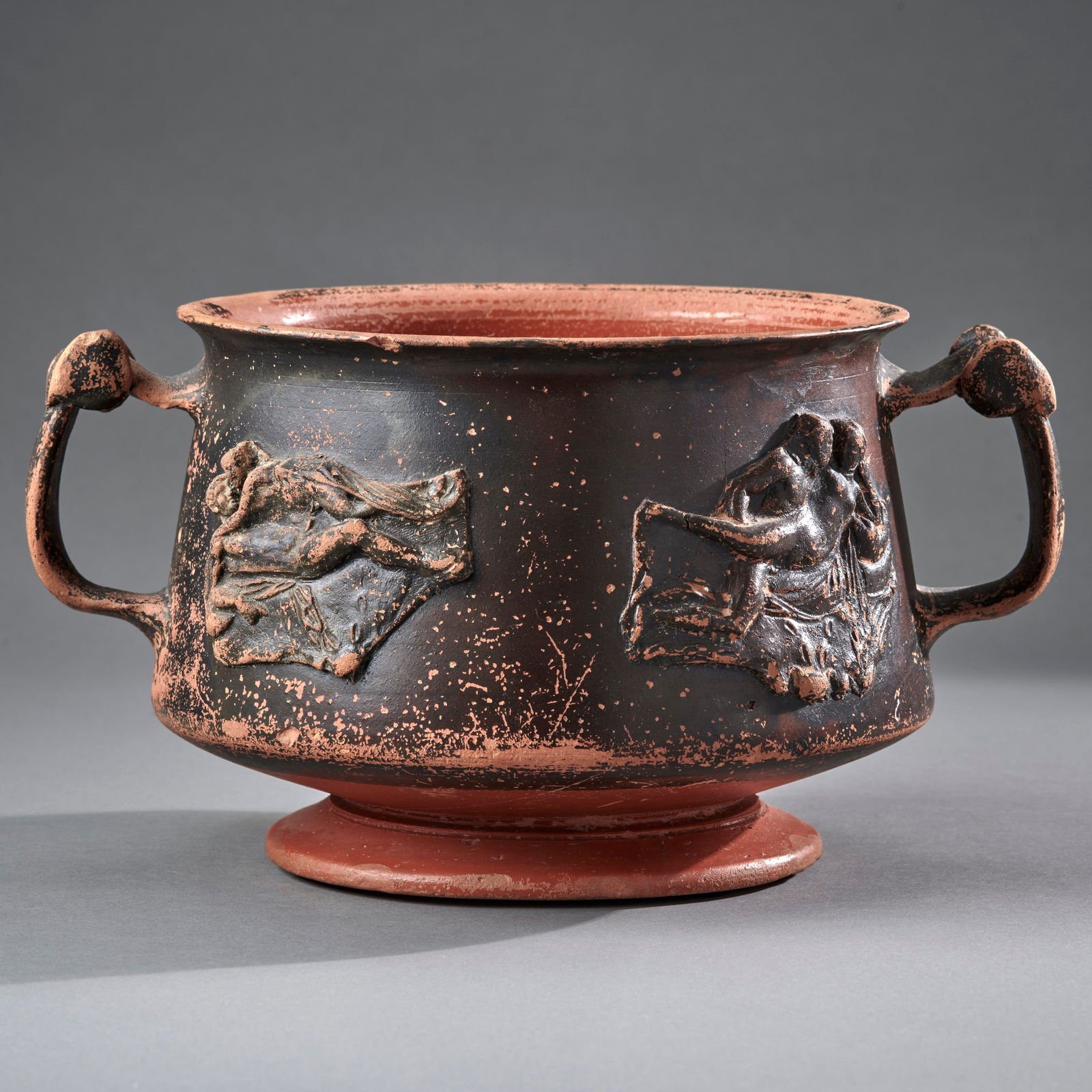 A Hellenistic Erotic Skyphos: Circa 2nd/1st Century B.C., the body with four applied moulded vignettes of couples, with black/brown glaze over redware. In good condition, intact with minor glaze loss and chips. Ht. 5, wd. 9 1/4 in