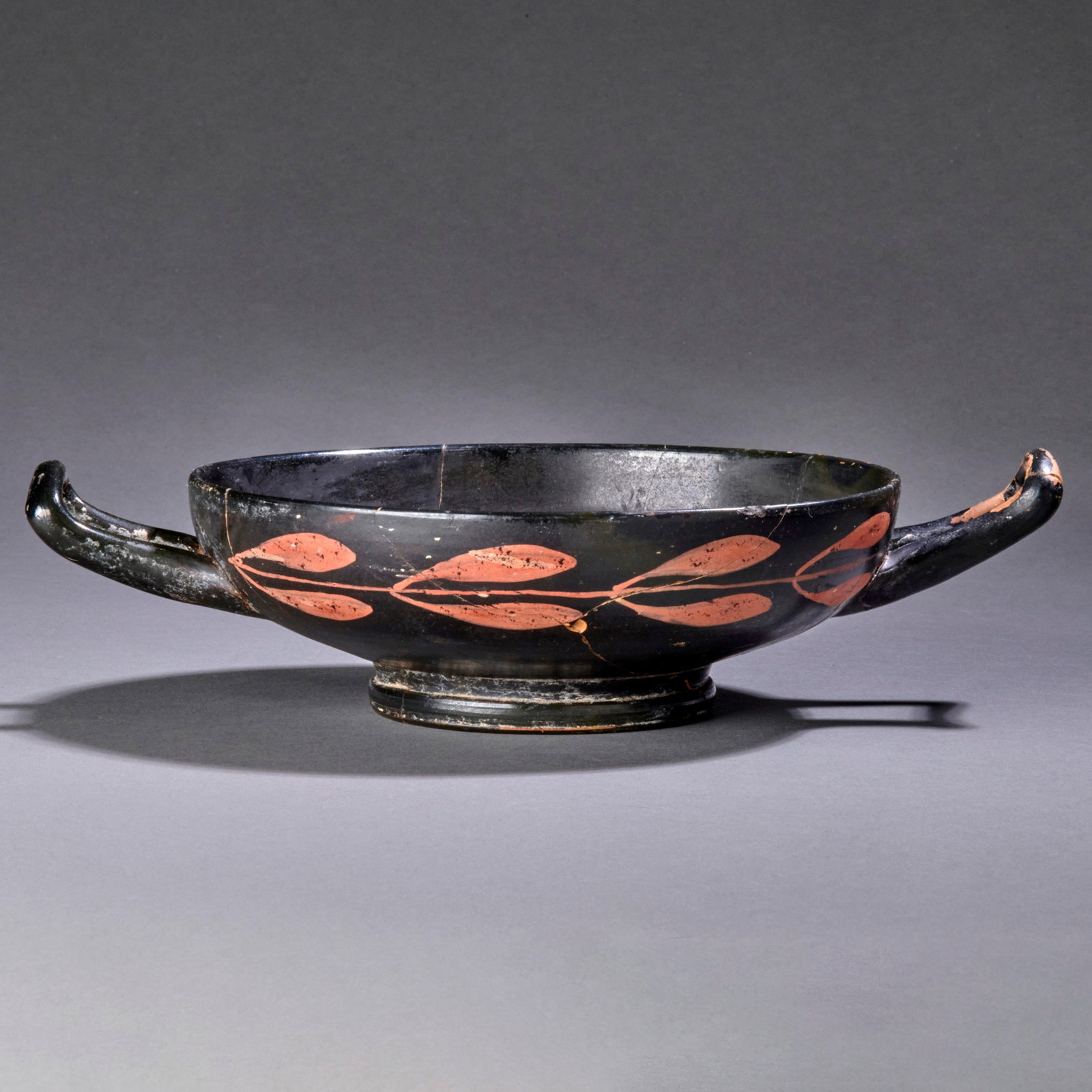 A Greek Xenon Ware Kylix: Apulia, Circa 4th century B.C., the central tondo with a swan in profile, flanked by olive branches. Wd. 9 5/8 in. Professionally repaired from numerous original fragments, with only a very small amou
