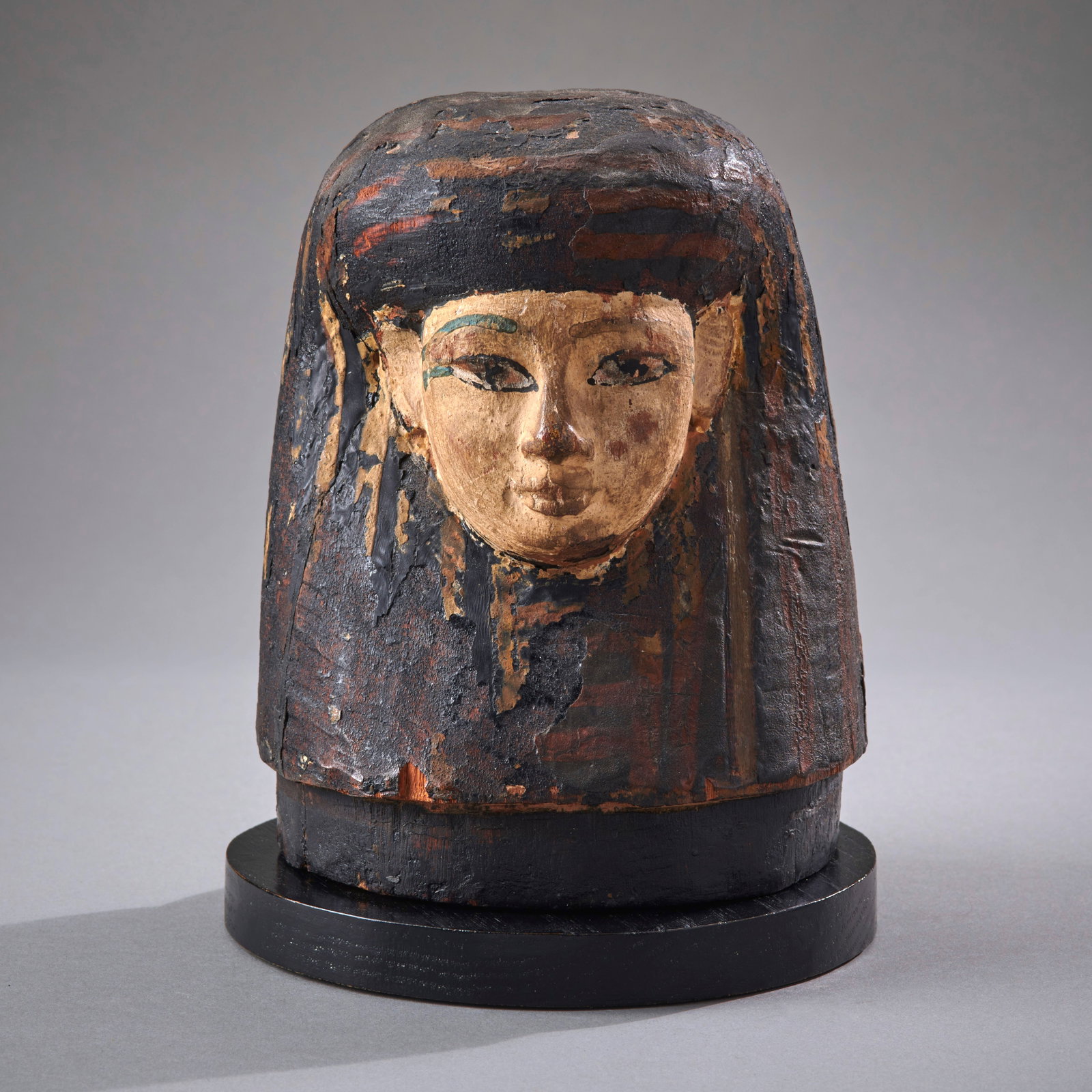An Egyptian Polychrome Wooden Canopic Jar Lid: 18th Dynasty, circa 1550-1292 B.C., a rare survival in wood from the golden age of Egyptian art, a male head wearing a tripartite striped wig, in good condition with pigment loss in places and minor a