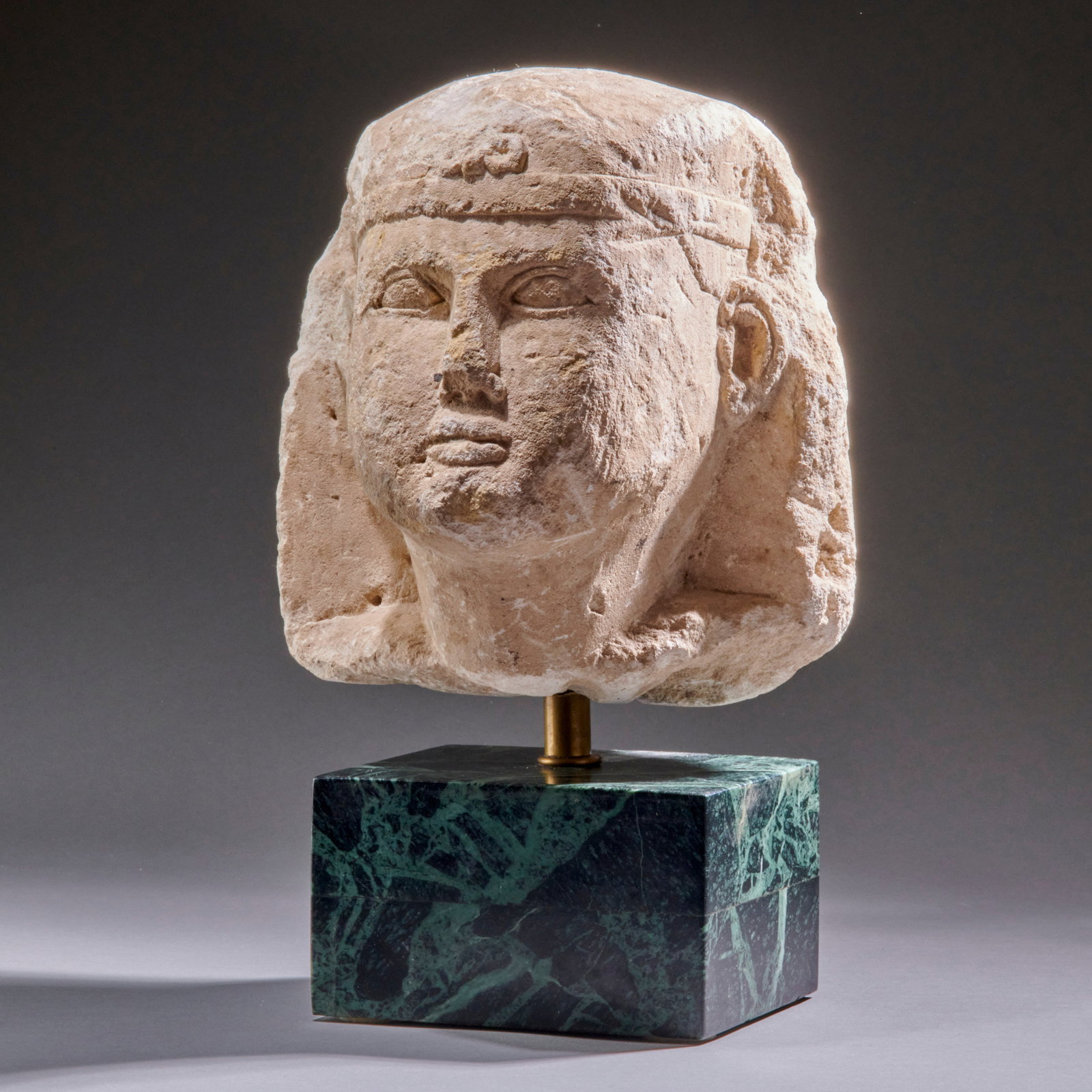 An Egyptian Limestone Head Of A Pharaoh: Ptolemaic period, circa 2nd-1st century B.C., possibly from a sphinx, depicted wearing the nemes headdress with a (mostly lost) central Uranus, the headcloth tucked behind the pronounced ears, the you