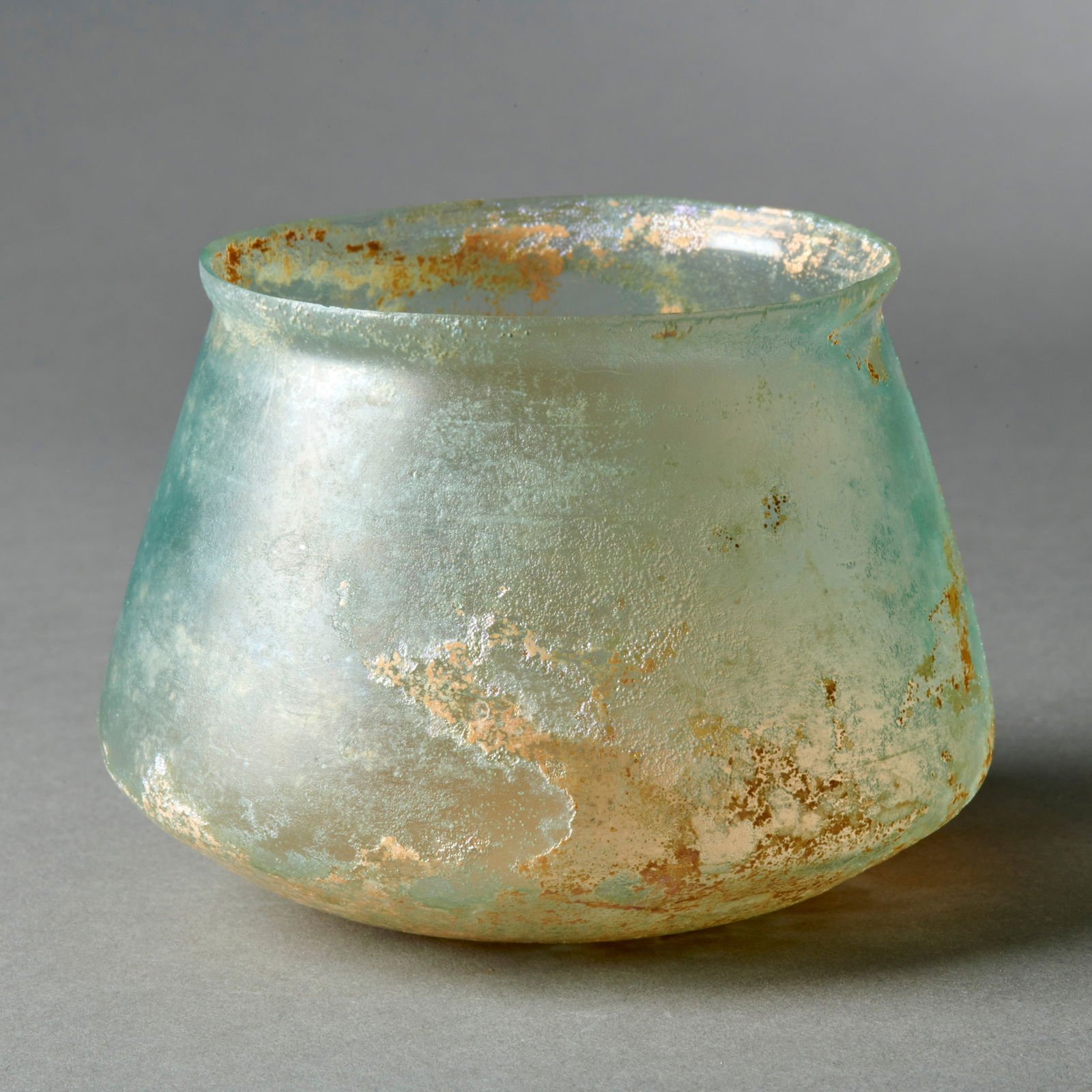 A Roman Glass Cup: Circa 1st/2nd century A.D., a fine, thinly walled carinated cup, with iridescent encrusted surface. In excellent intact condition. Ht. 2 9/16 in. 6.4 cm. dia. 3 1/2 in. 8.8 cm. Provenance: Purchased a