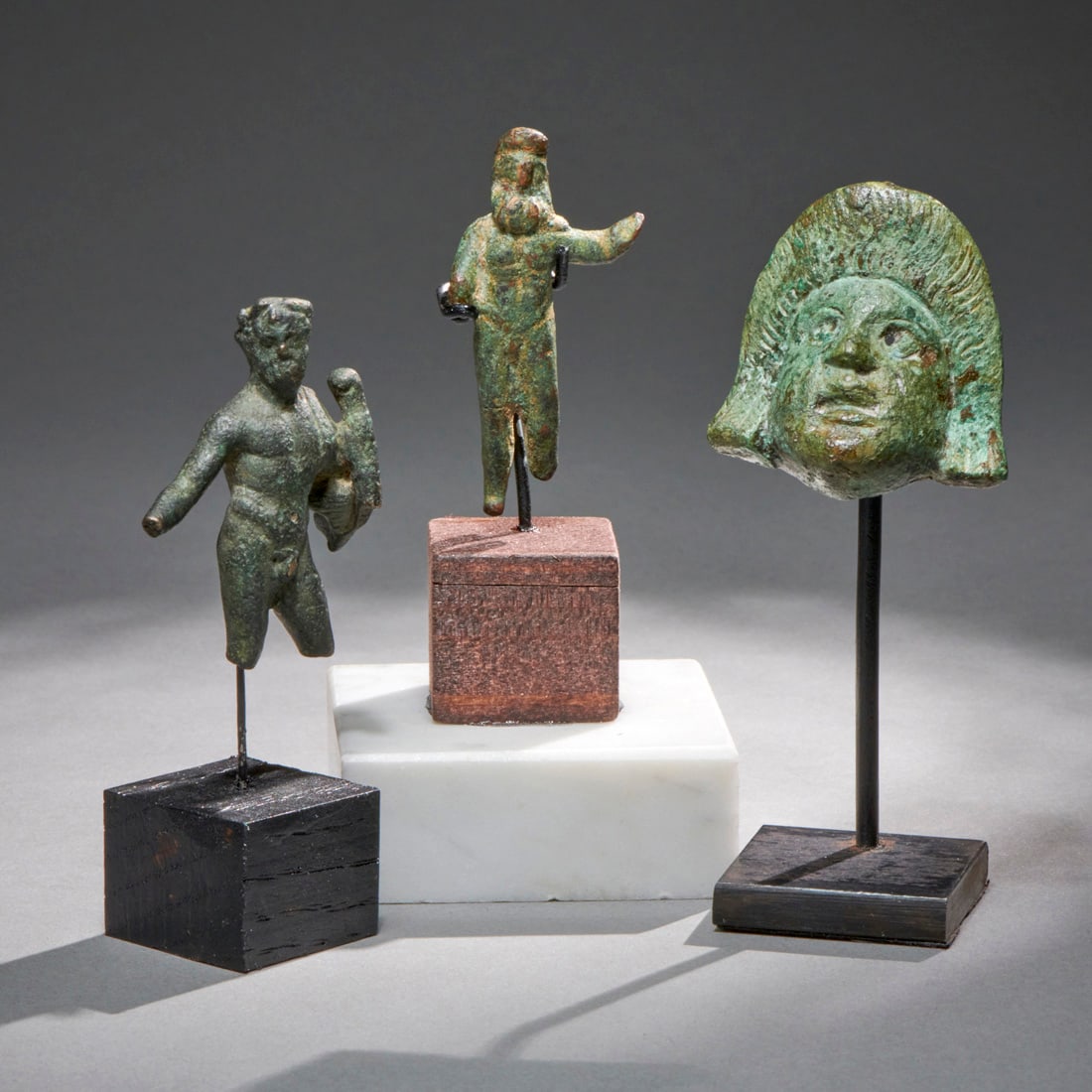 Three Small Roman Bronze Figures: Roman Empire, ca. 1st- 2nd century a.d., two figures, likely Hercules and a theatre mask applique. Custom bases. Good condition with losses as shown.Ht. Of mask without stand 1 1/2 in. Shipping within