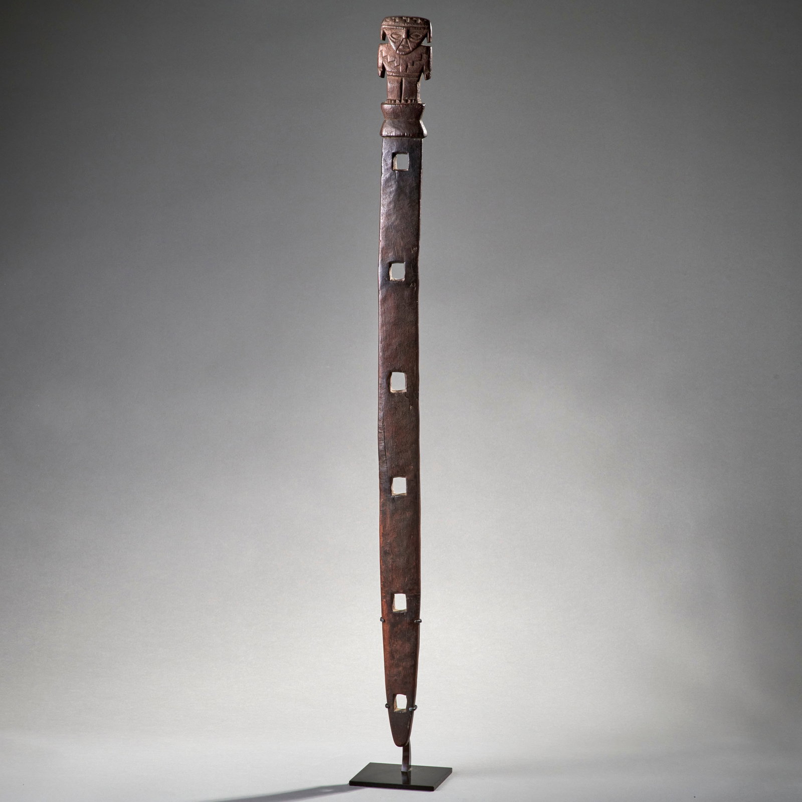 A Chimu Carved wood loom post: Chimu culture, Peru, c. 1000-1400 A.D., wood, the carved wood post with piercings, with a figural finial depicting a priest, mounted on a custom bronze base. Lg. 32 in. Shipping within the continental