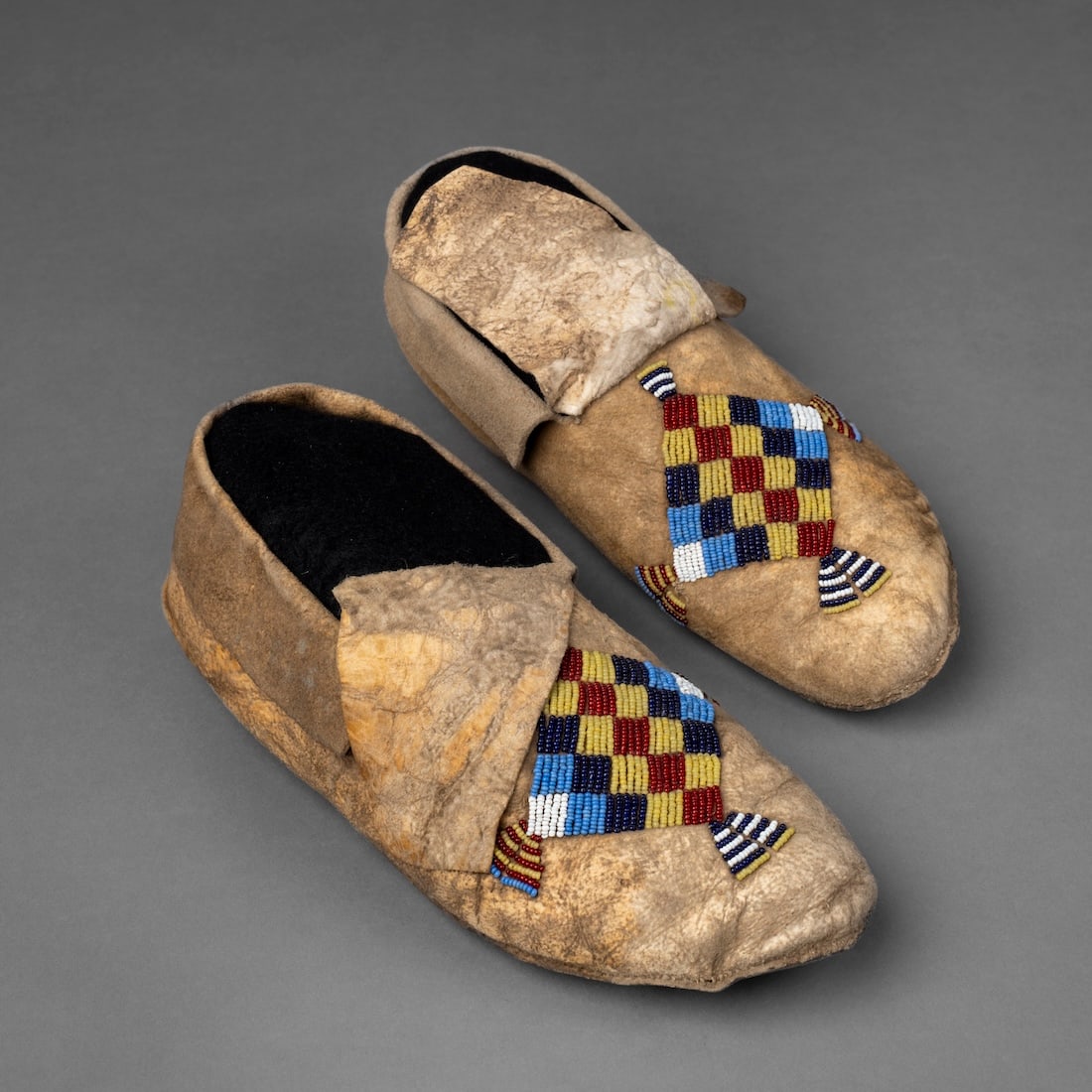 A pair of Plains beaded hide moccasins: Fourth quarter 19th century, the buffalo hide soles, with soft hide uppers with multicolored bead decoration on the vamps. Lg. 9 7/8 in.