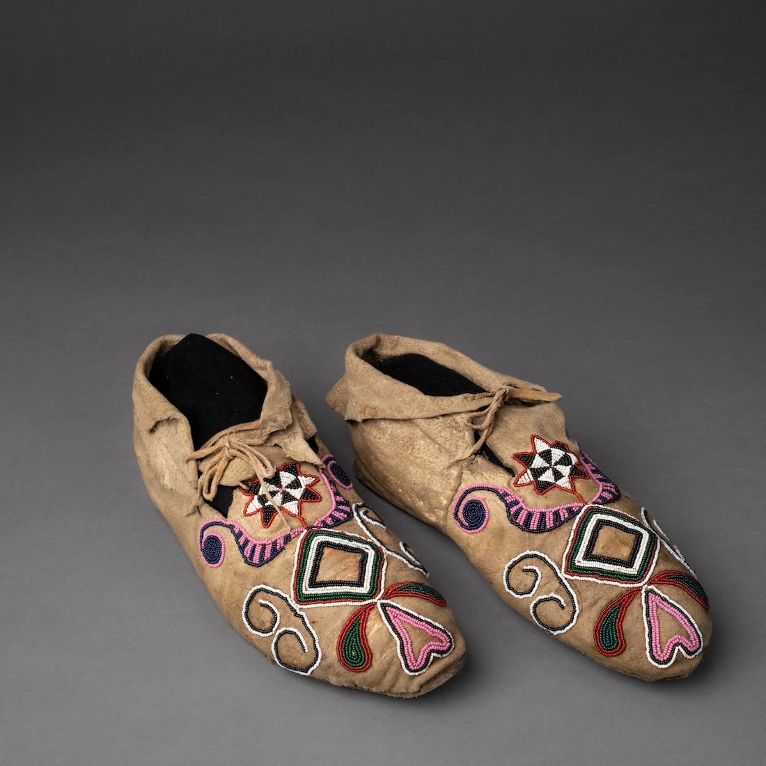 A Pair of Plains Beaded Hide Moccasins: Dakota, fourth quarter 19th century, the hard hide soles, with the soft hide vamps decorated with multicolored beaded designs, with soft hide cuffs. Lg. 9 1/2 in.