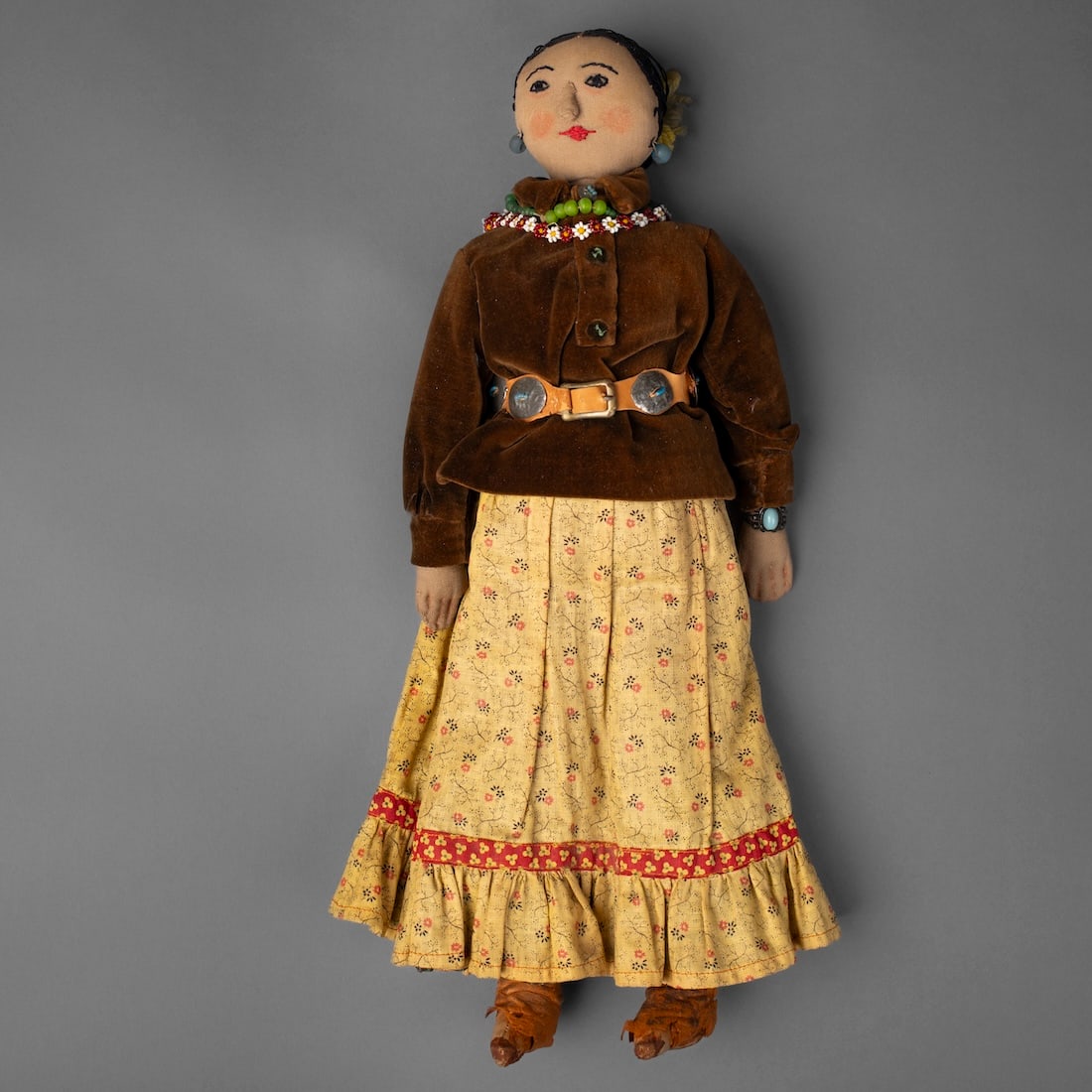 A Navajo doll: Wearing traditional dress, with a concha belt, a turquoise cuff bracelet, necklaces and earrings, loss to the hide boots. Lg. 16 1/2 in. Provenance: Private collection, Santa Fe, New Mexico; Traphagen