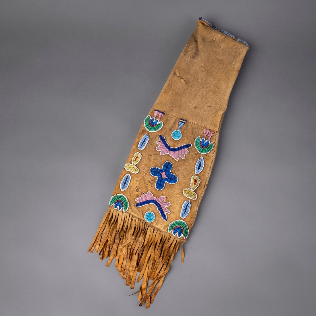 A Northern Plains beaded hide pipe bag: Circa 1870s, Wind River Crow, the soft hide bag, decorated on one side with multicolored floral designs, with hide fringe from below, with beaded roll opening, missing fringe ends. Lg. including fring