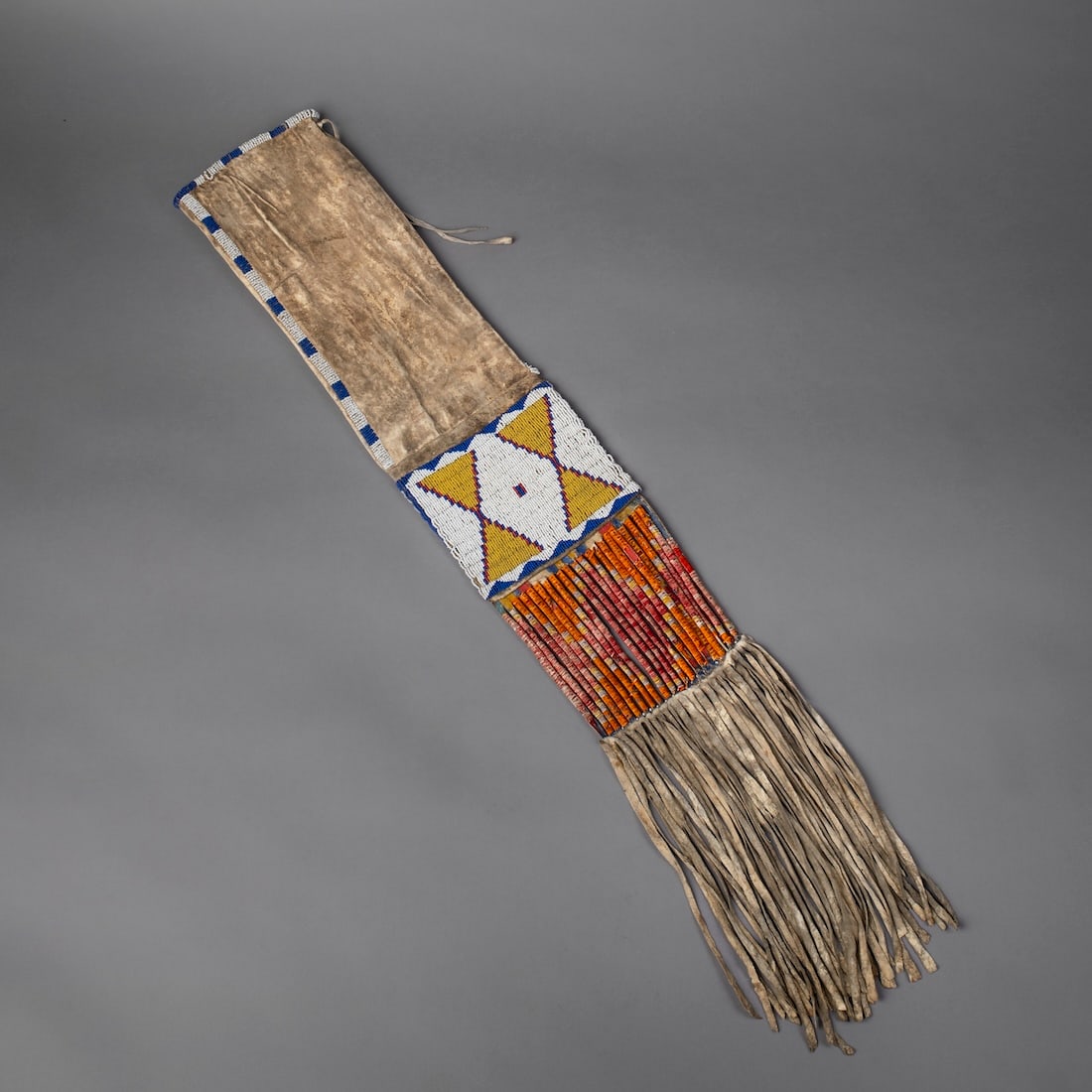 A Plains beaded hide pipe bag: Lakota (Sioux), circa 1880s, very finely beaded panel on each side, a beaded strip up one side and roll beaded opening, with repurposed parfleche lower slat-panel with quill decoration, and long hide