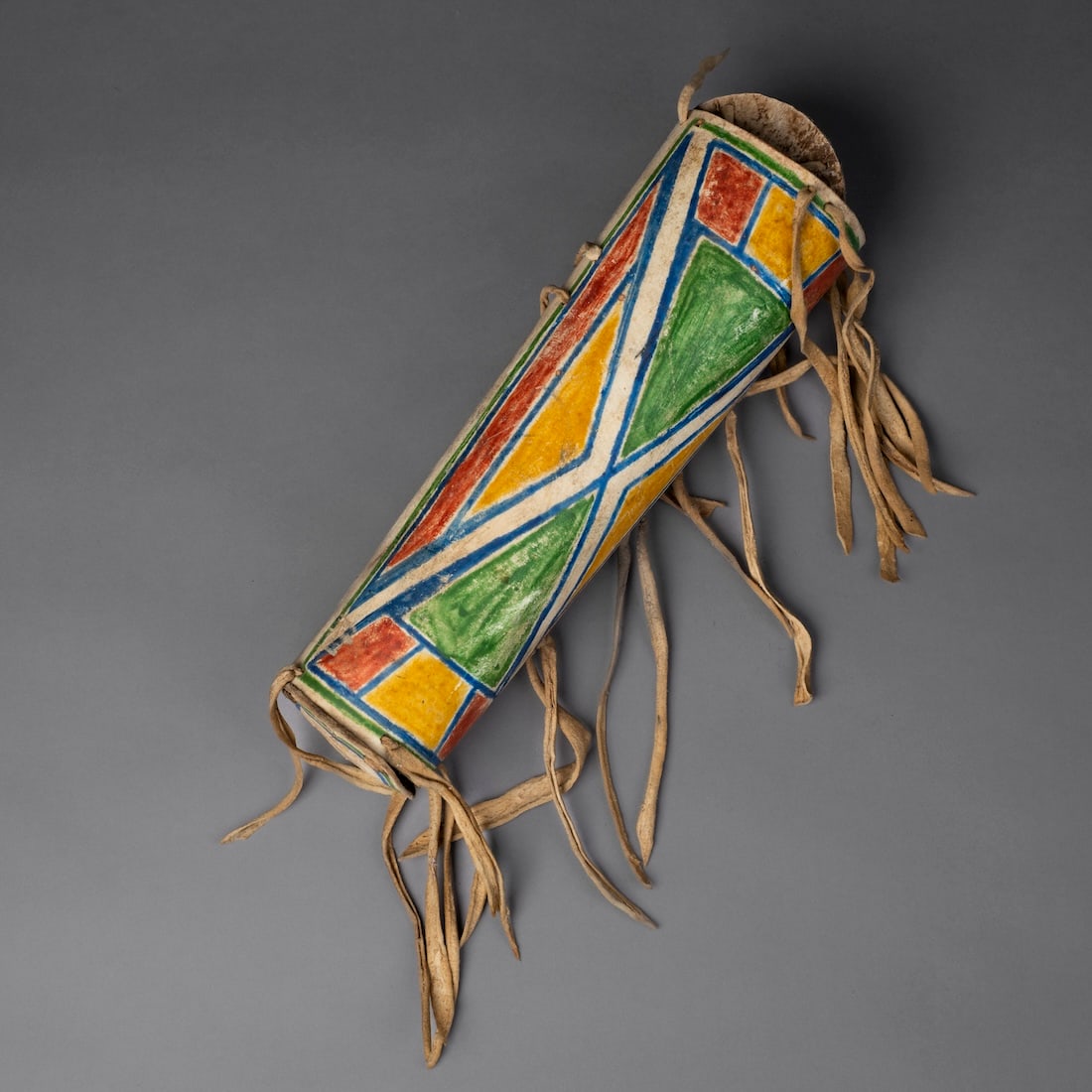 A Northern Plains parfleche cylinder: The hide container decorated on one side with multicolored geometric designs, with a decorated round lid at both ends, and long hide tassels. Lg. 13 in.