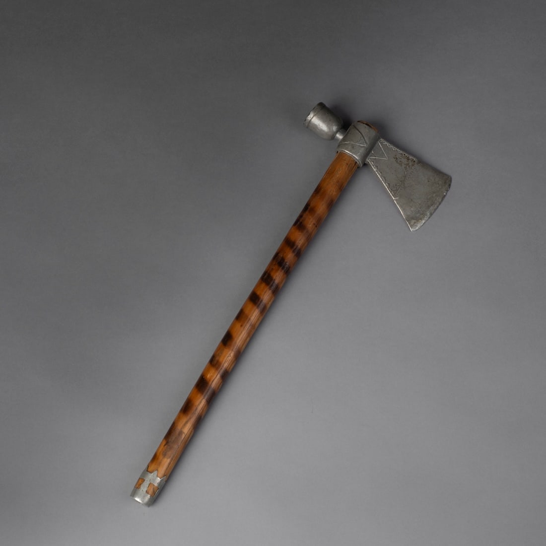 A Great Lakes pipe tomahawk: Mid 19th century, the pewter head with ornamented designs, the wood haft with burnt ring markings and a pewter cast mouthpiece. Lg. 15, ht. of head 5 1/8 in. Provenance: Richard Pohrt Jr. Ann Arbor, M