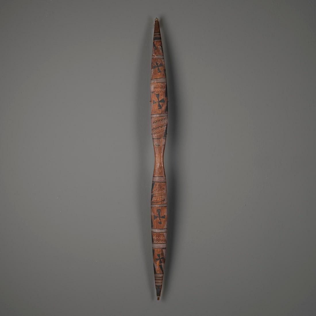 A Modoc painted bow: 19th century, painted on either side of the waisted grip with mirror-image registers of complex bands, wavy lines, dots and star devices, with gut string attached, and with a metal wall mount. Lg. 38
