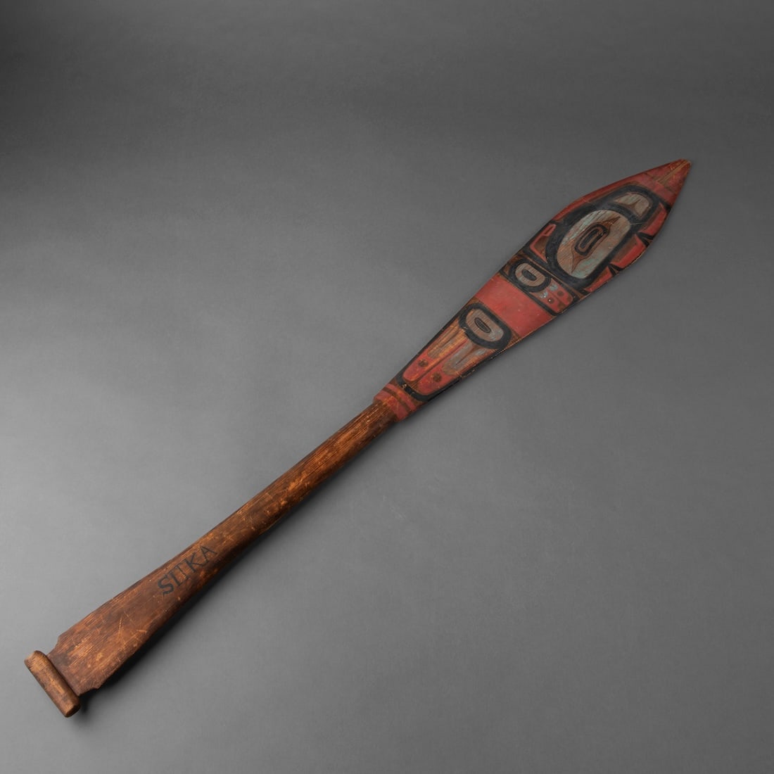 A Northwest polychrome paddle: Tlingit, circa 1870s, the cedar wood carved dance paddle with very finely painted multicolored clan formalize designs on both side, with “Sitka”, painted on the shaft. Lg. 37 1/2 in.